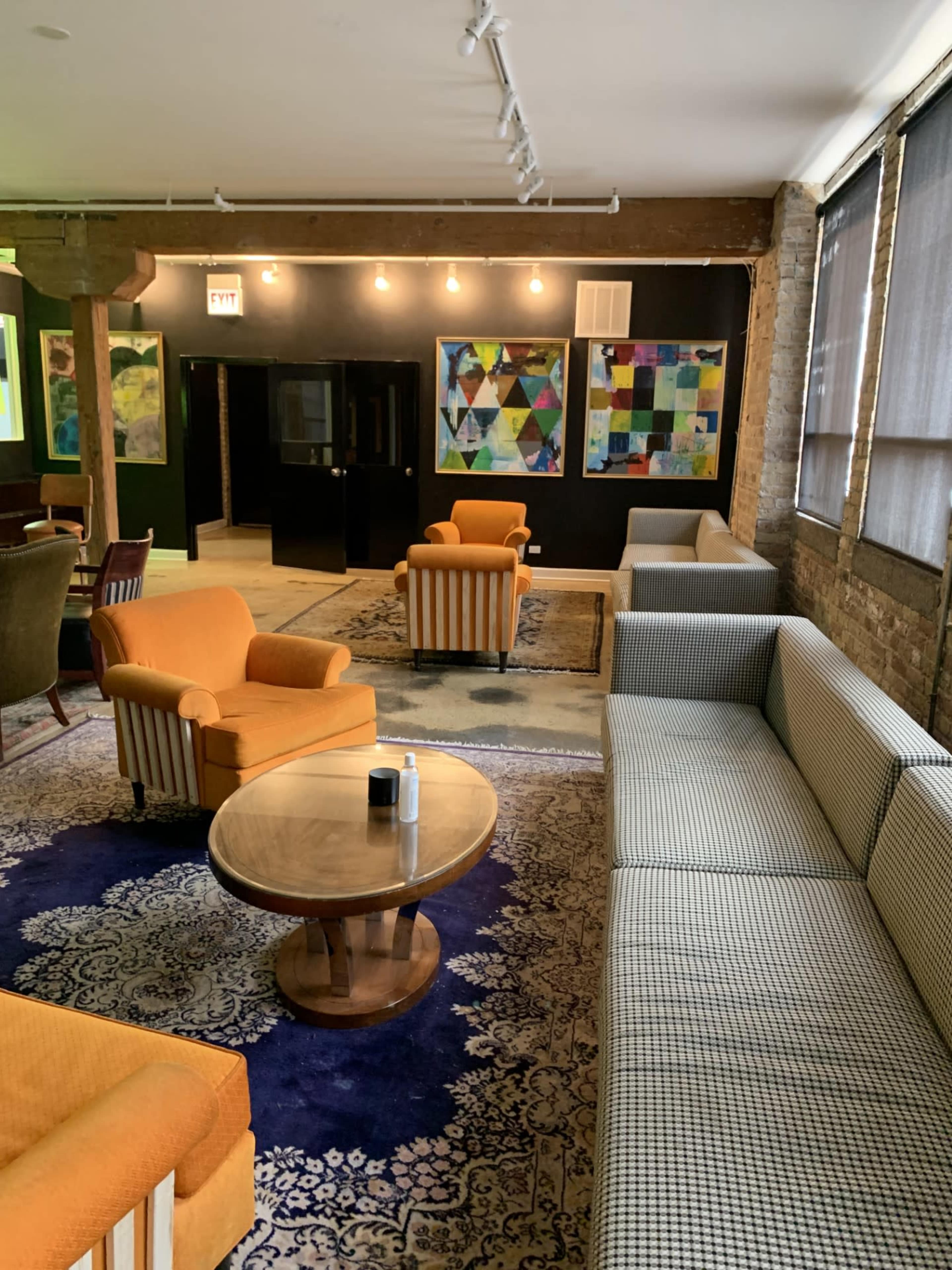 A stylishly furnished lounge area with orange armchairs, a patterned sofa, a round table, and colorful artwork on the walls.
