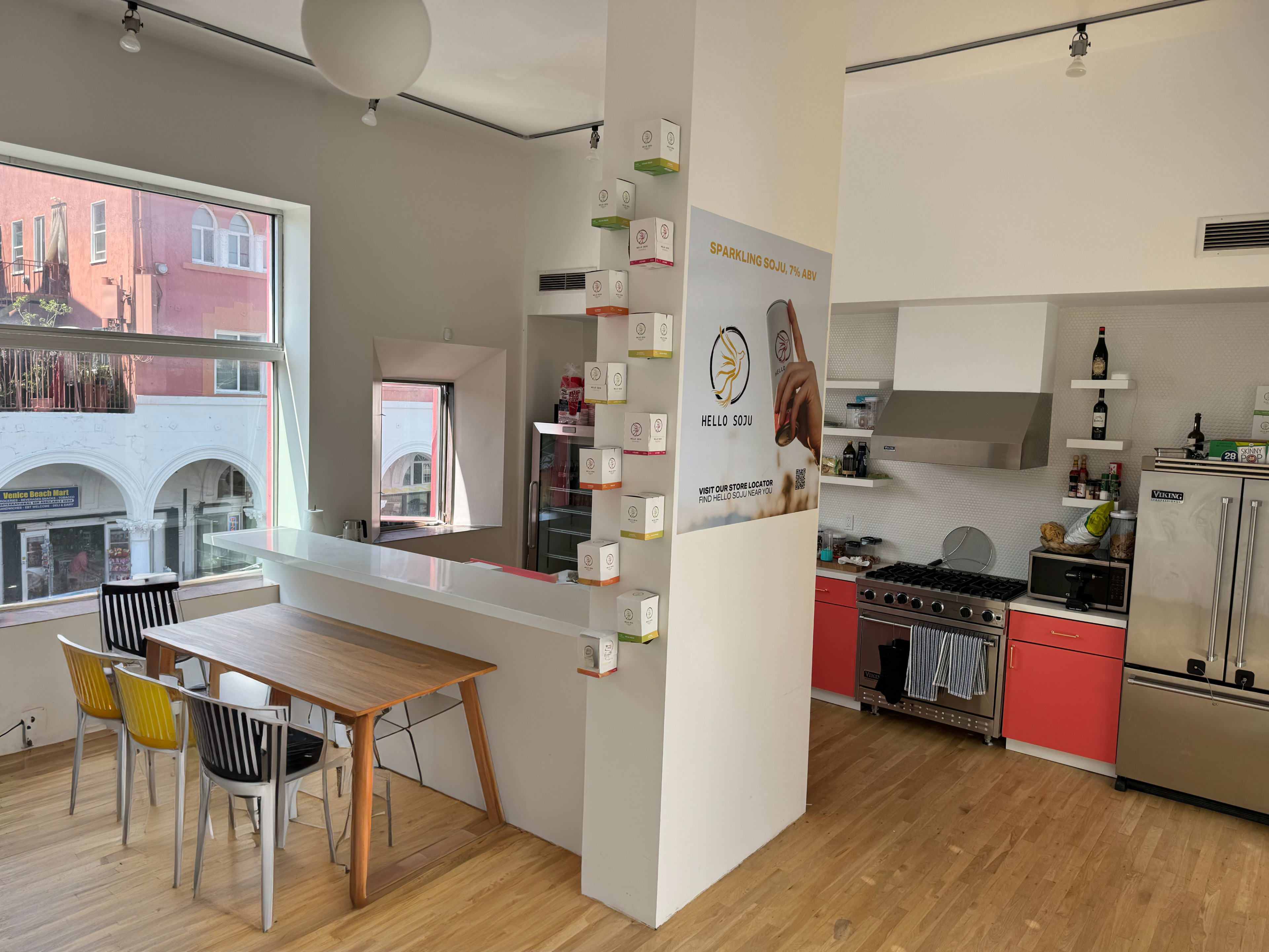 A modern kitchen with a dining table, colorful chairs, and a wall displaying product boxes alongside a promotional mural.