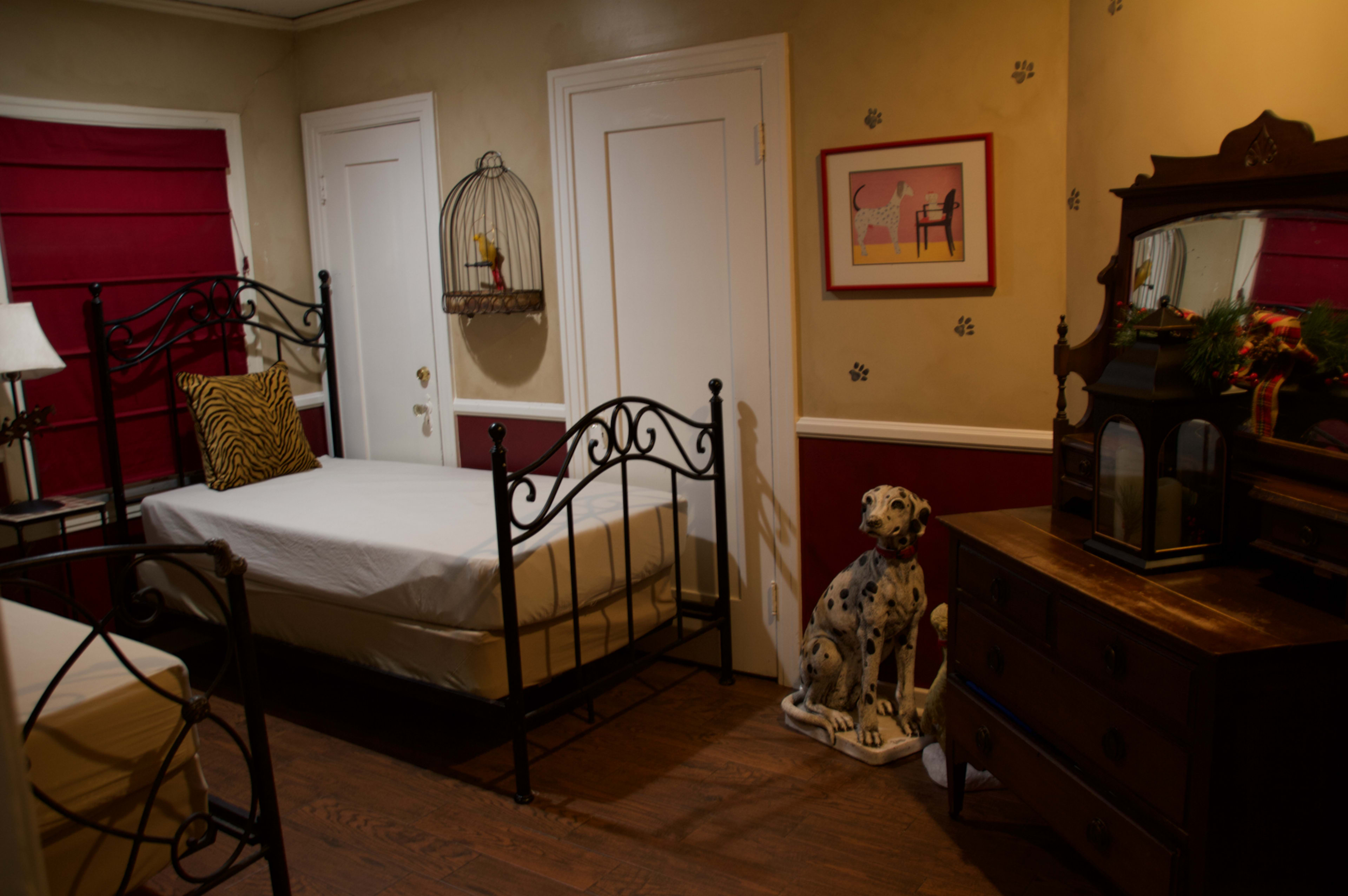 The room features two metal-framed beds, a dresser, and a decorative dog statue, with red and beige walls.