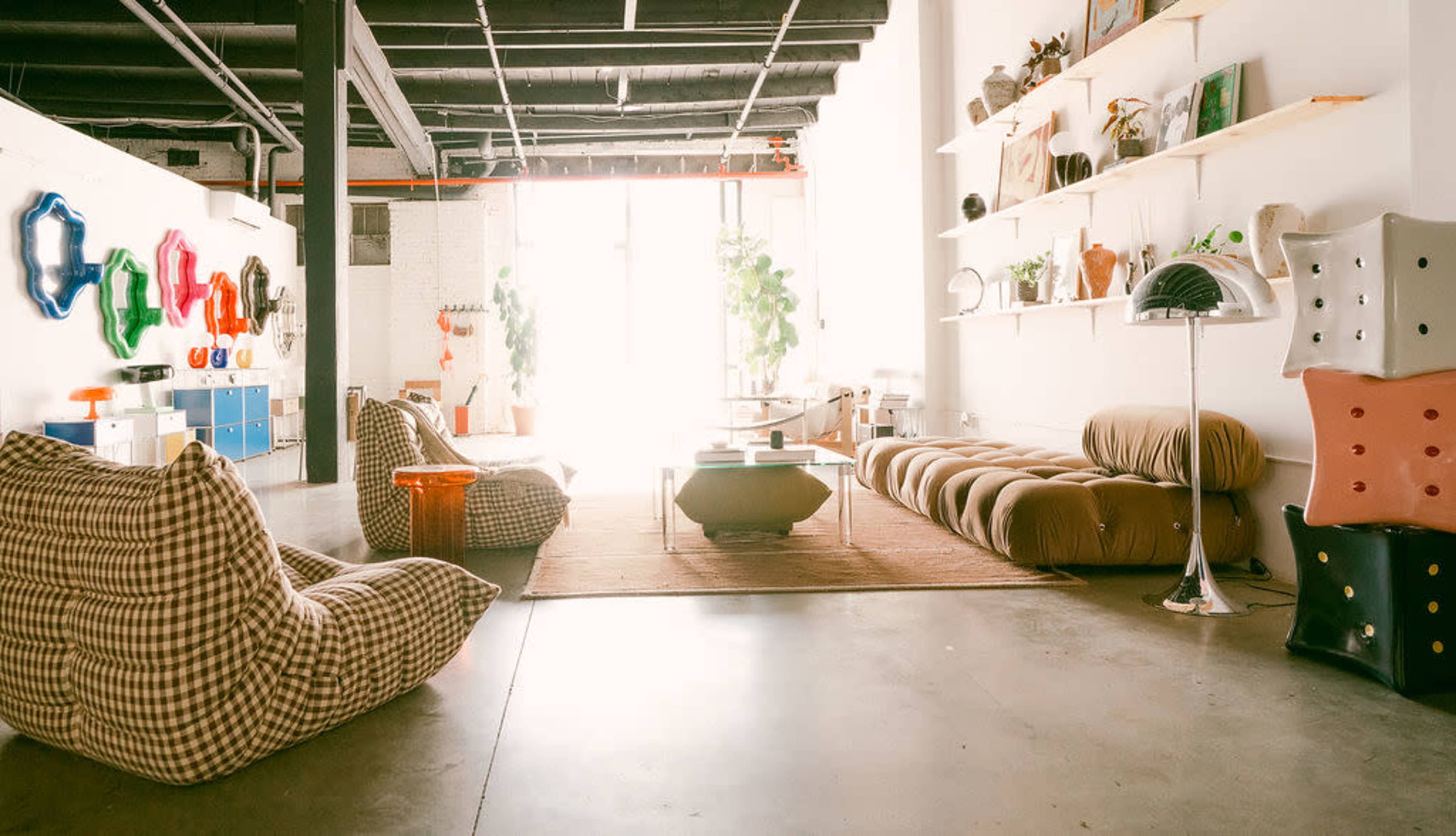 The image shows a spacious interior decorated with various modern furniture pieces, including bean bags, a large sofa, and shelving displaying objects and plants.