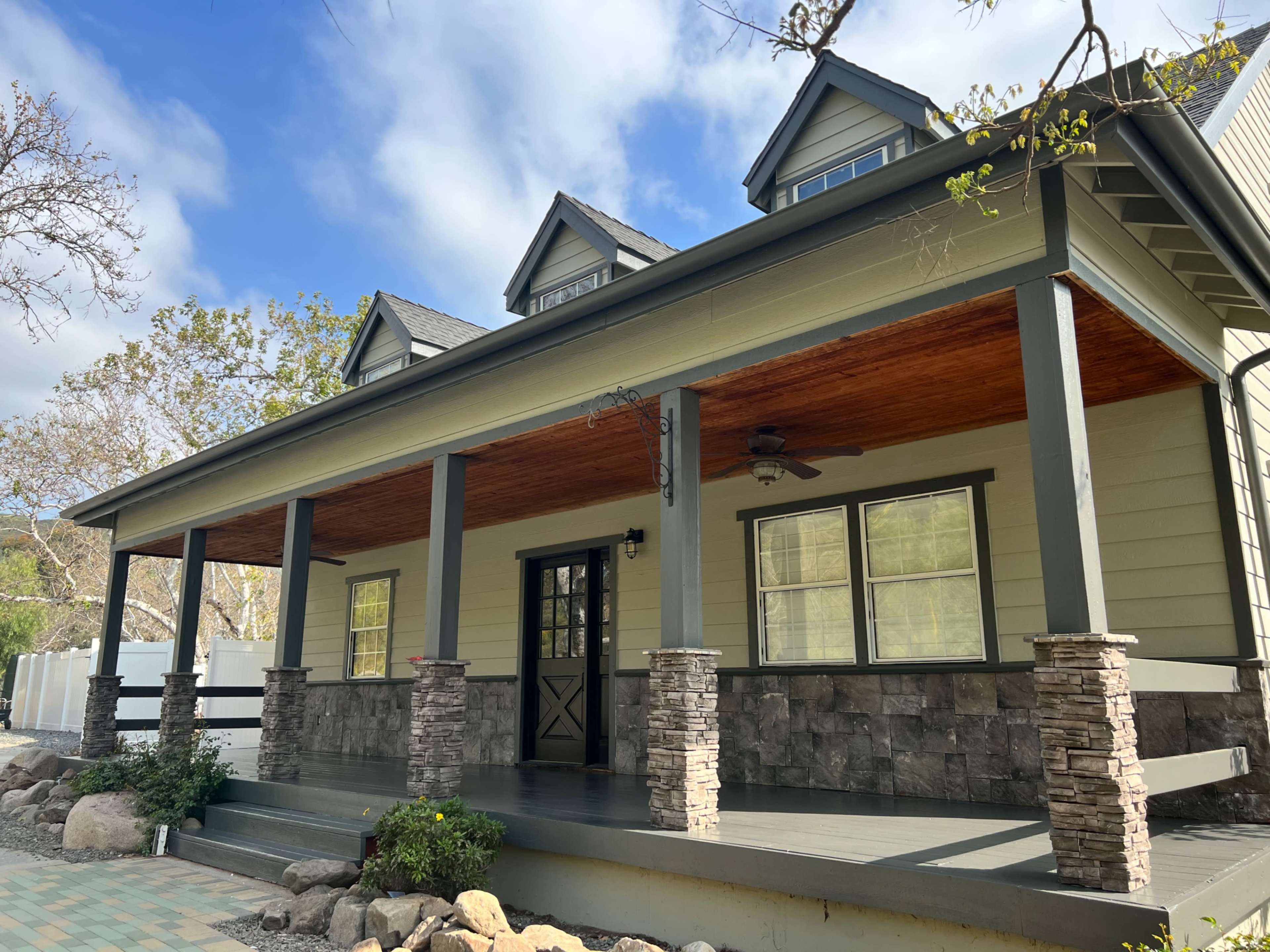 A modern house with a front porch supported by stone pillars and a wooden ceiling.