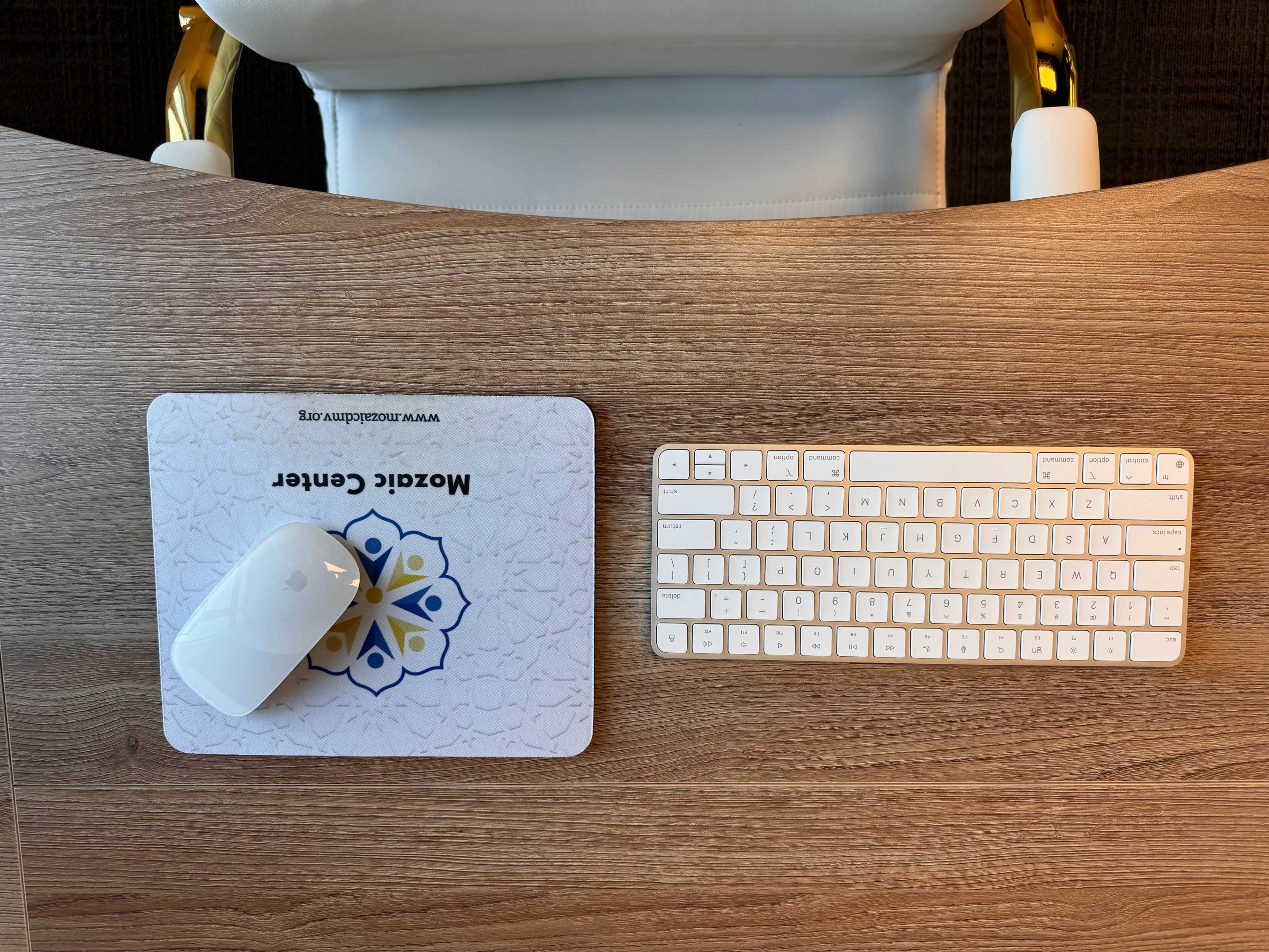 An office workspace features a keyboard and mouse on a wooden desk.