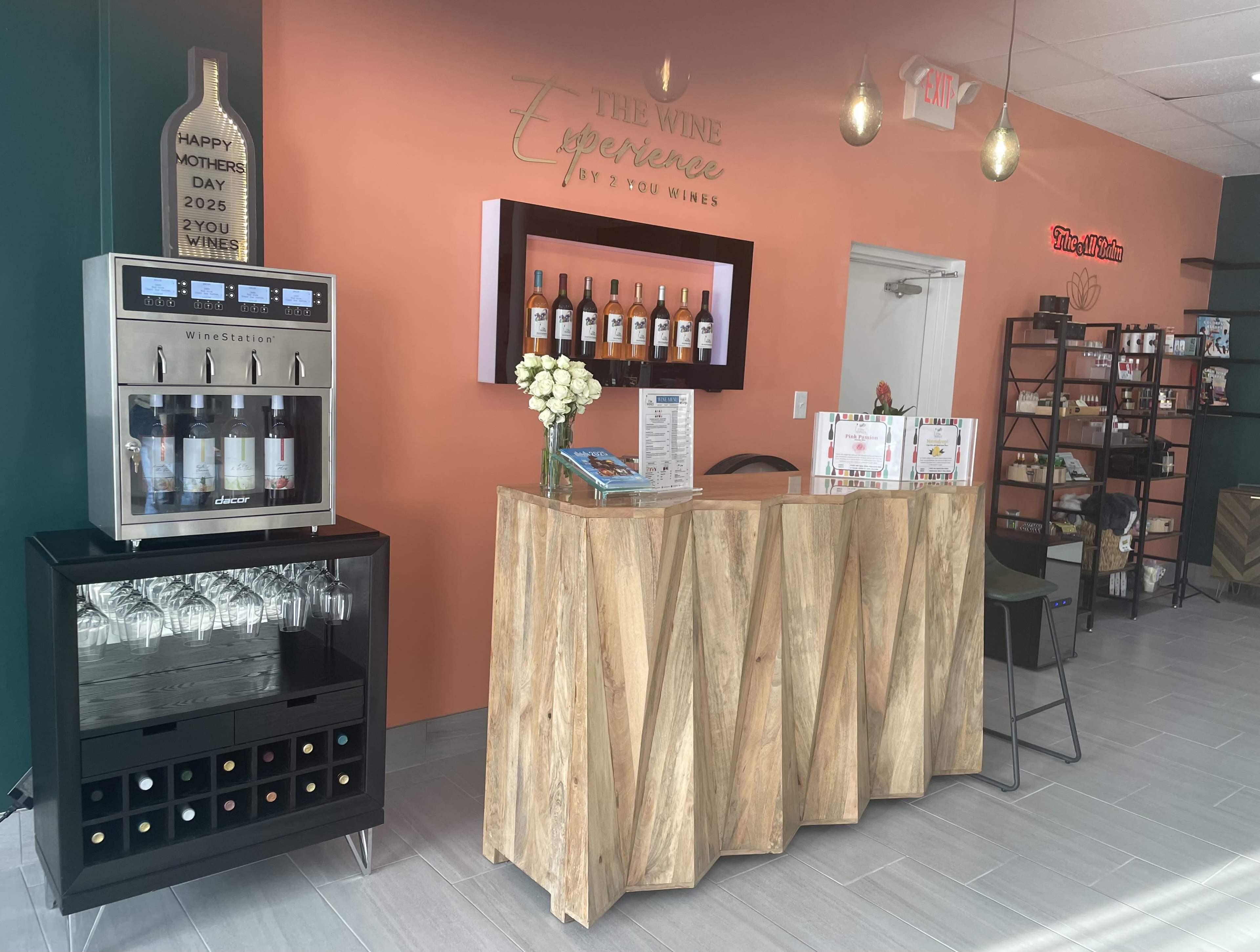 The image shows a wine tasting room with a wooden bar, wine dispensing machine, and shelves displaying bottles, against an orange wall.