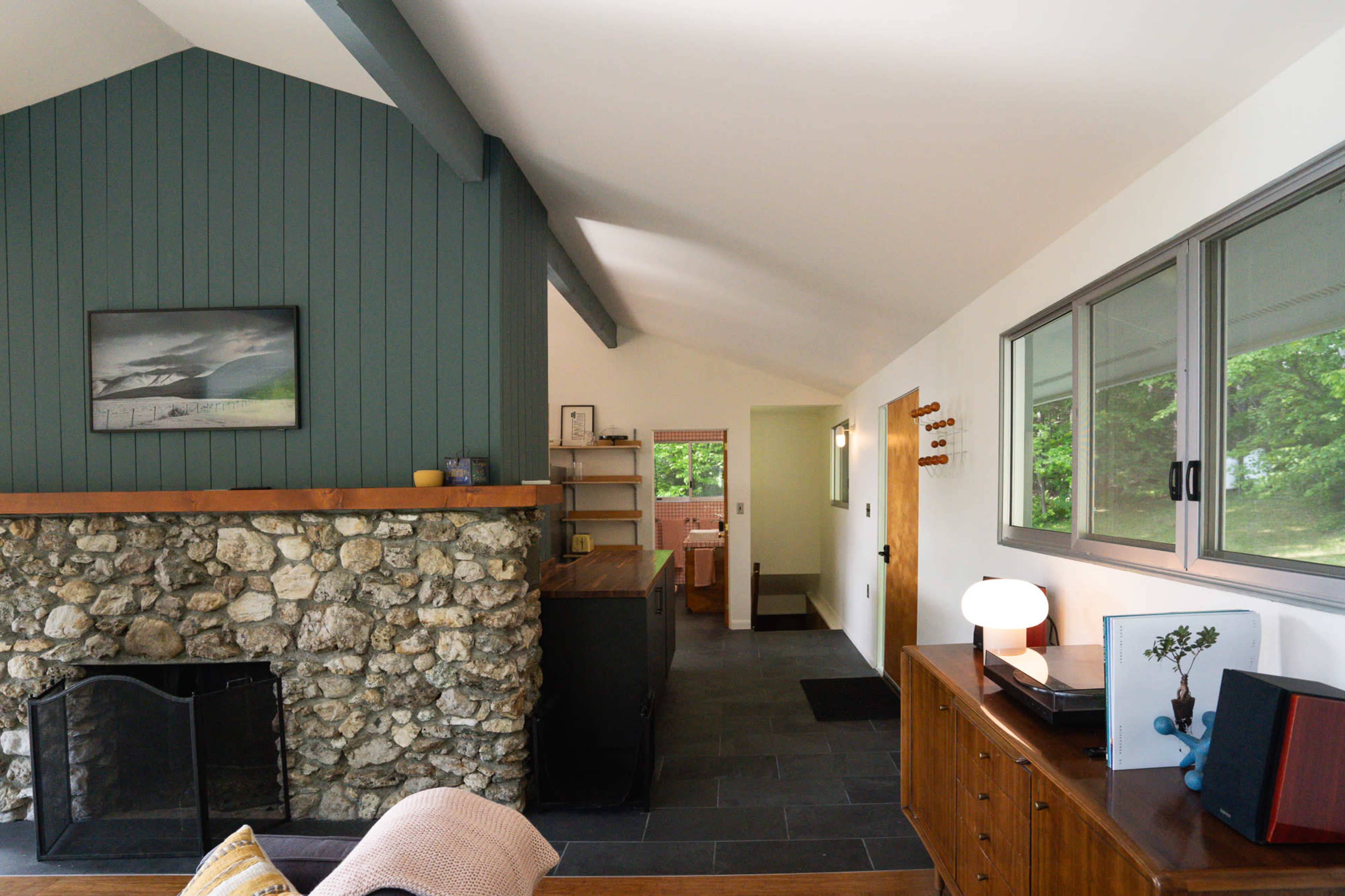 The interior scene features an open living space with a stone fireplace, wooden furniture, and large windows allowing natural light.