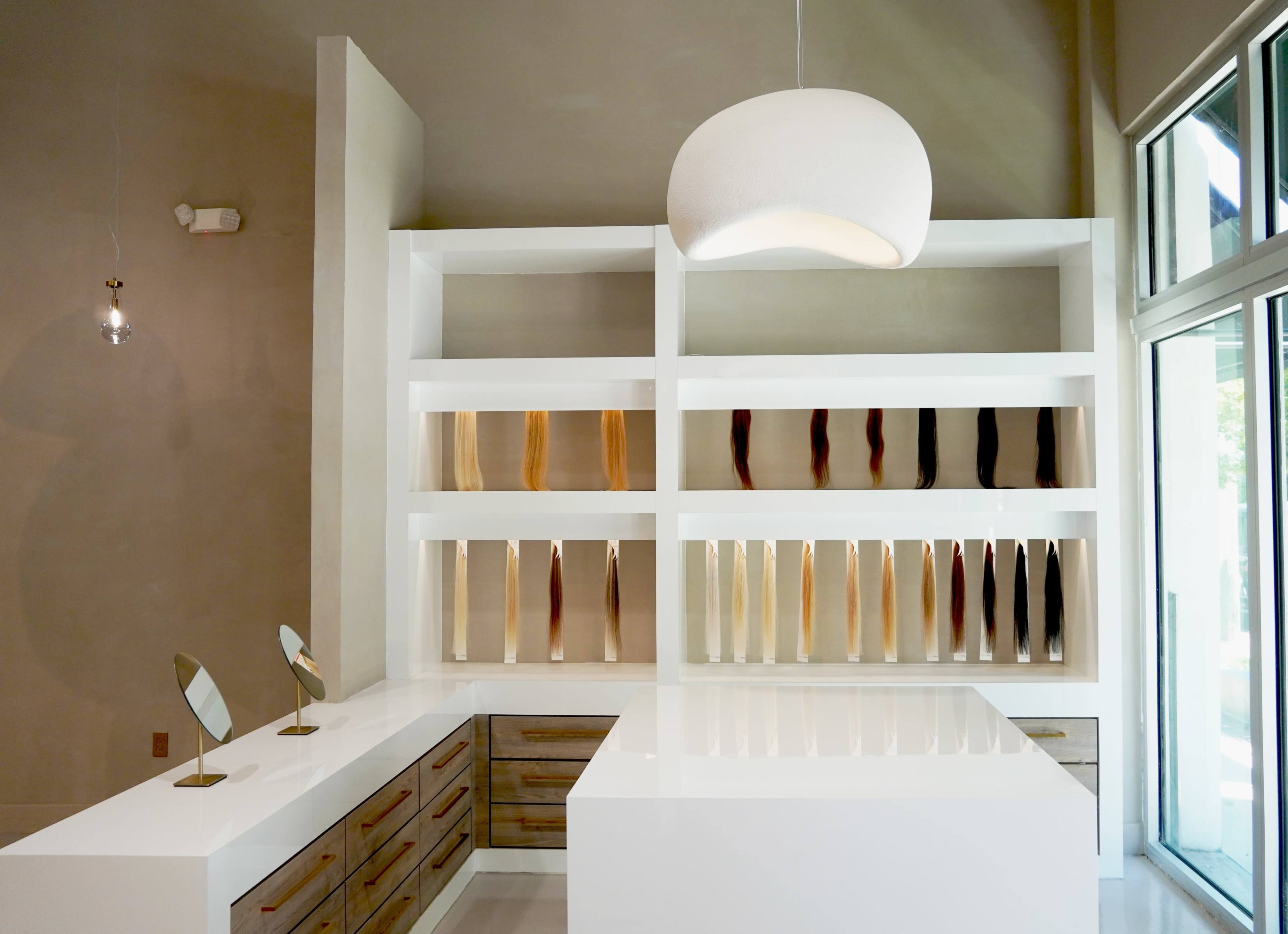 The image shows a modern interior of a shop featuring a white display shelving unit with various colored products, a sleek counter, and large windows letting in natural light.