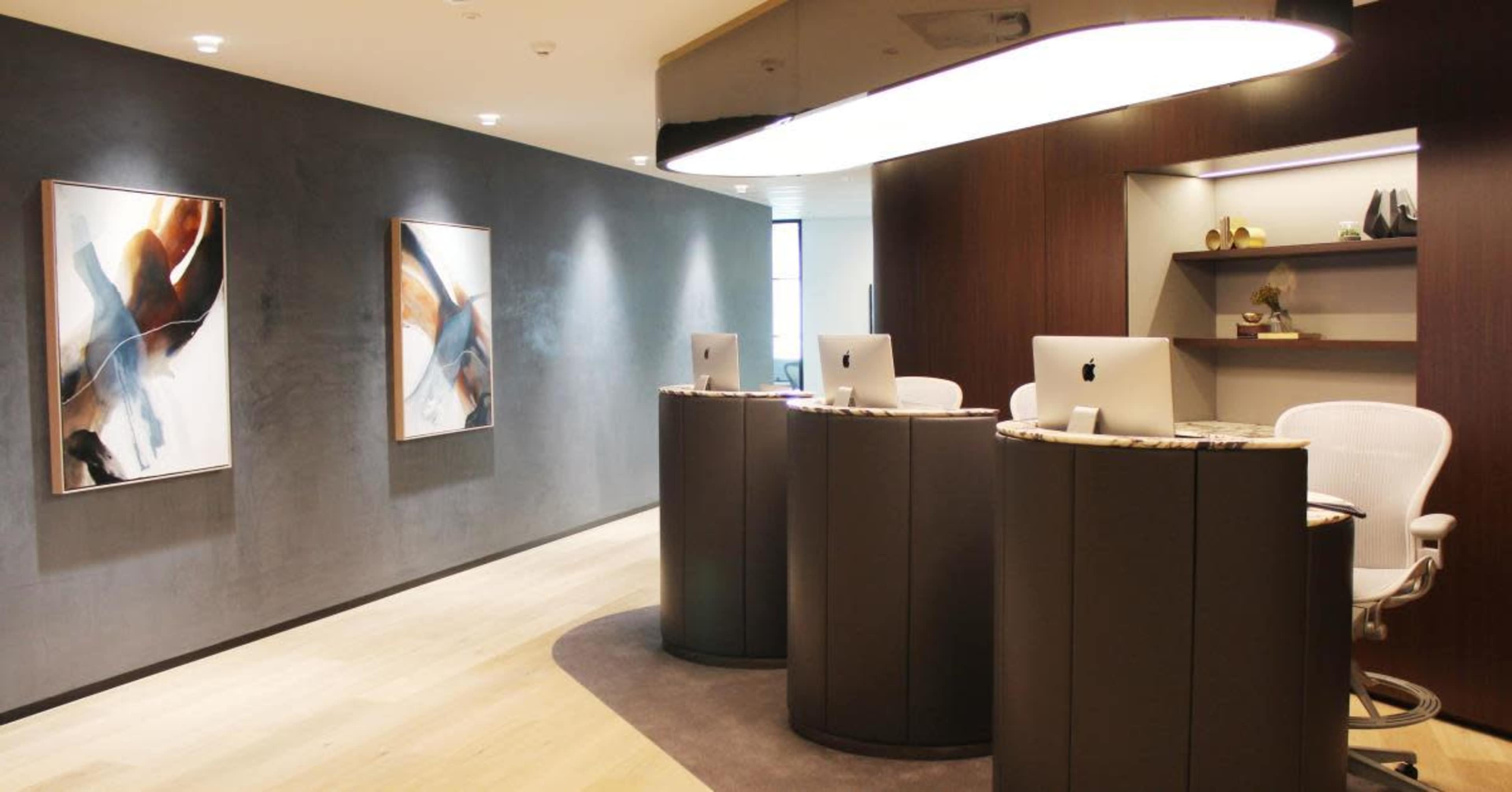 The image shows a modern reception area with two curved desks, computers on each, and abstract artwork on the walls.