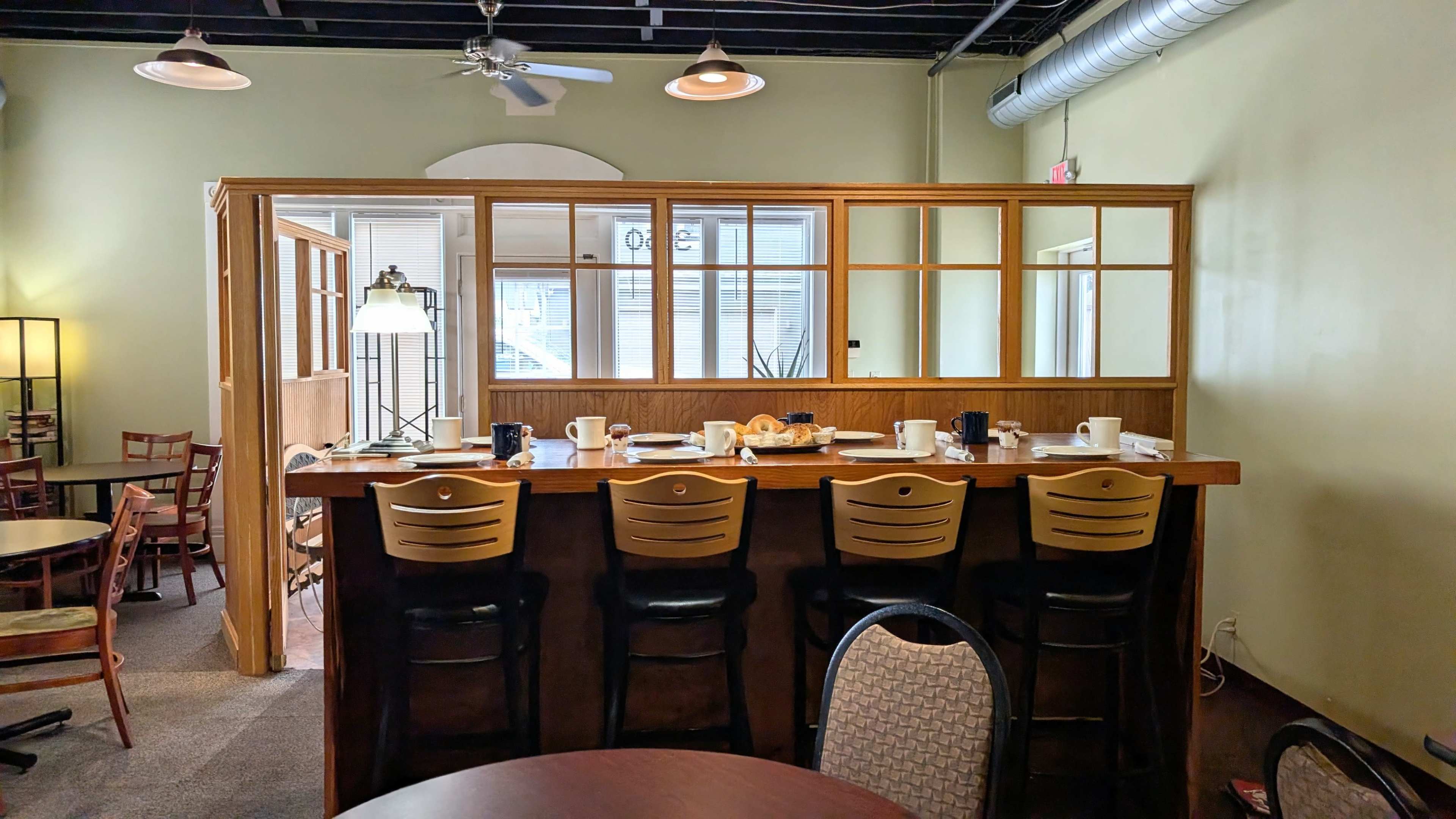 The image shows a coffee shop interior featuring a counter with several empty stools and tables set for dining.