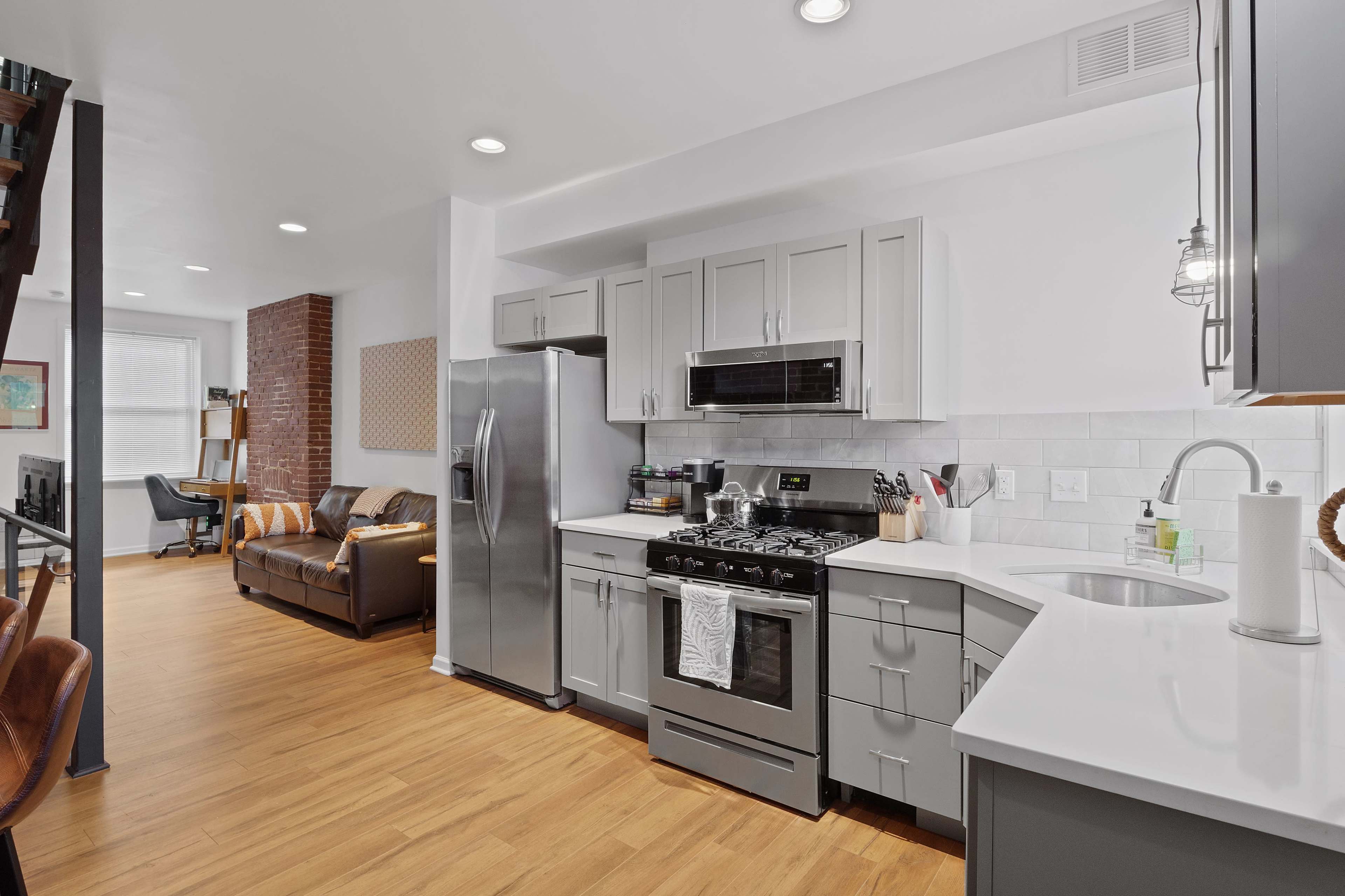 A modern kitchen features stainless steel appliances, gray cabinetry, and an open layout that connects to a living area with a brown couch.