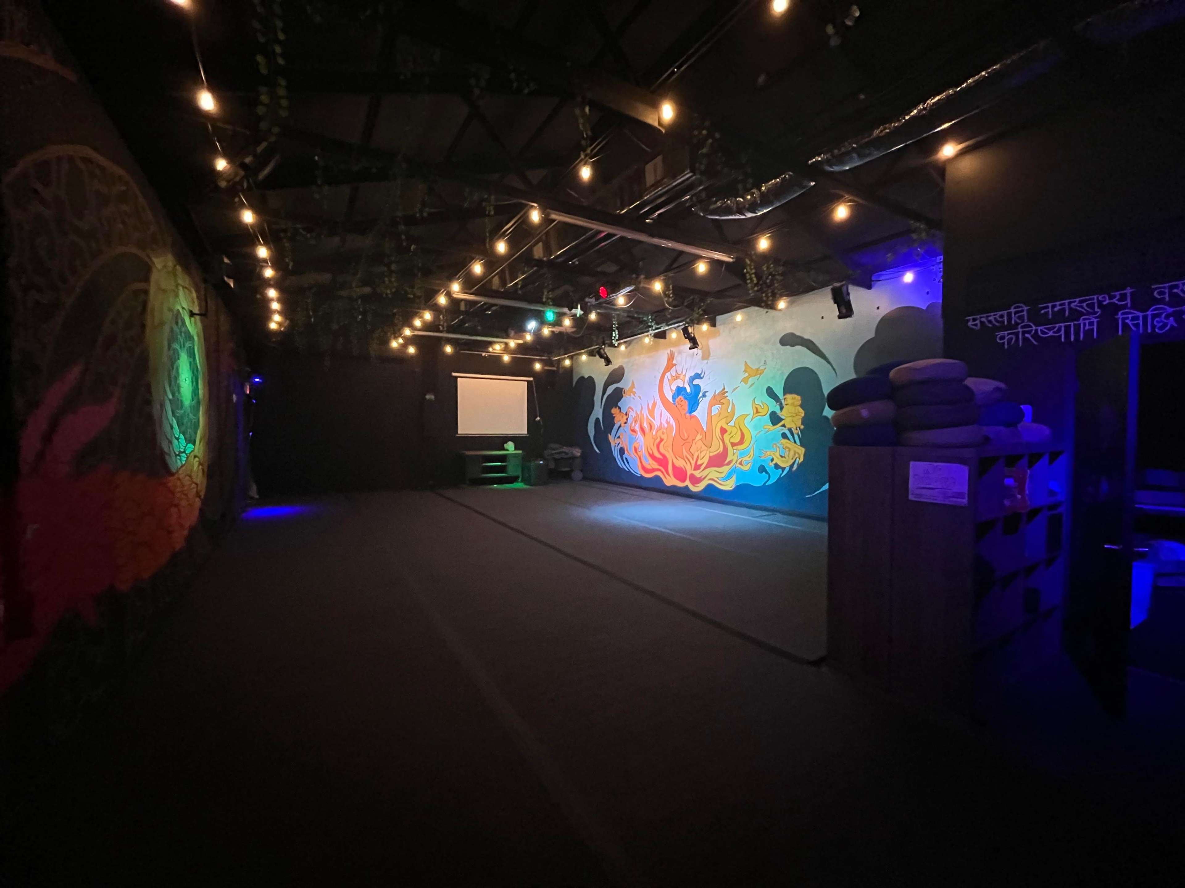 A dimly lit room with colorful murals on the walls and a projection screen, set up for an event or gathering.