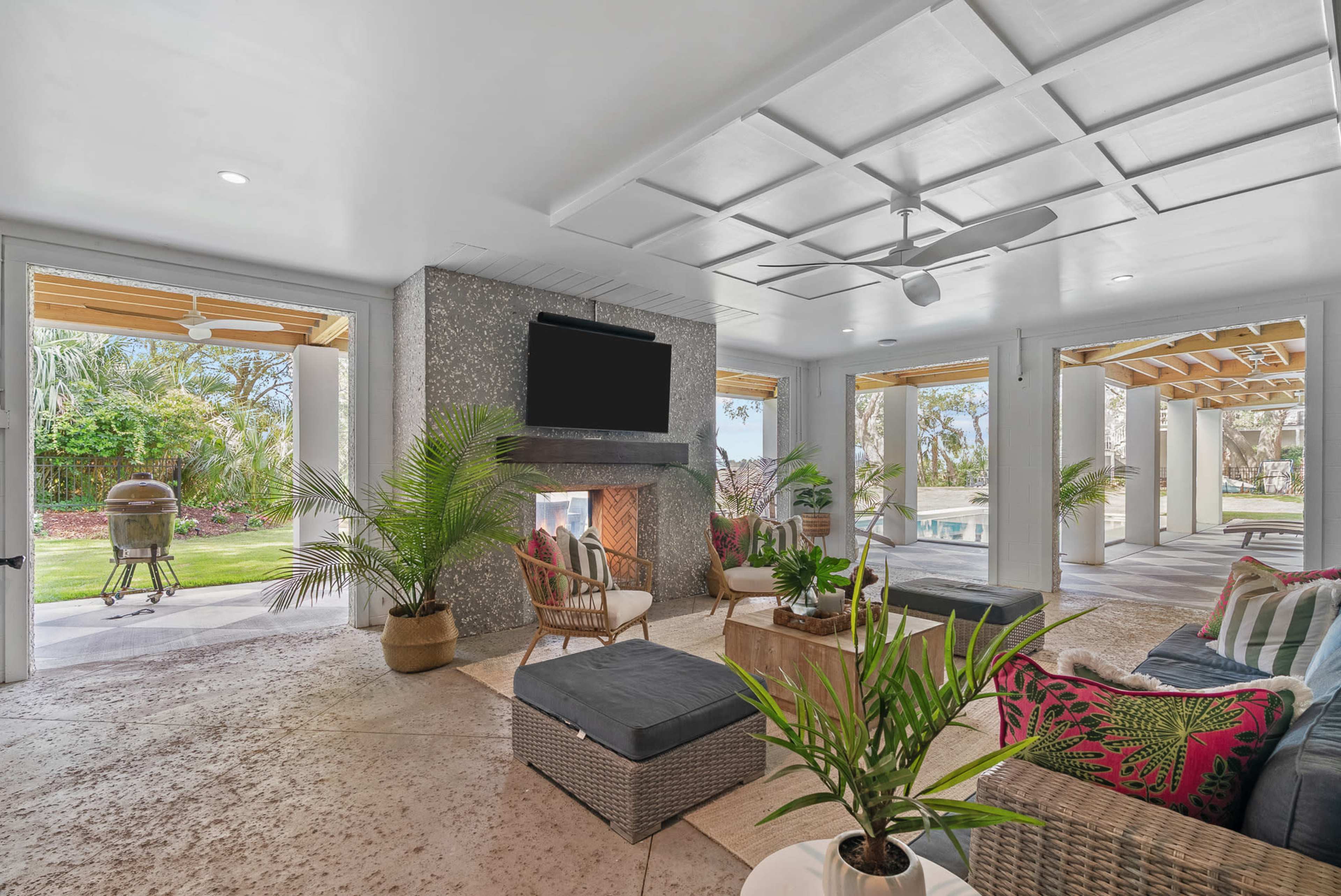 A spacious indoor lounge features a stone fireplace, two ceiling fans, and sliding doors leading to a lush outdoor area.