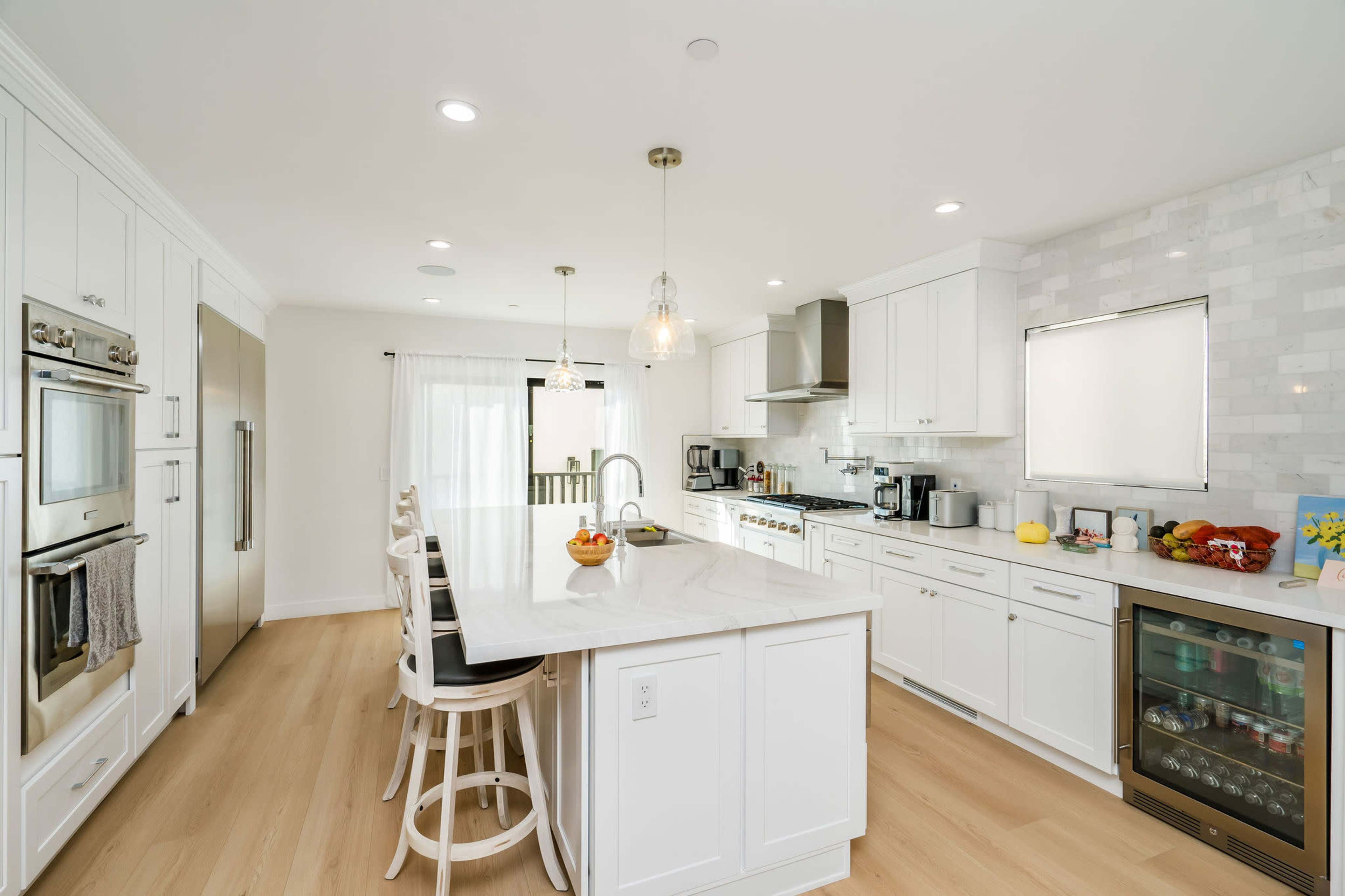 The kitchen features white cabinetry, a large island with bar seating, and stainless steel appliances against a light-colored backdrop.