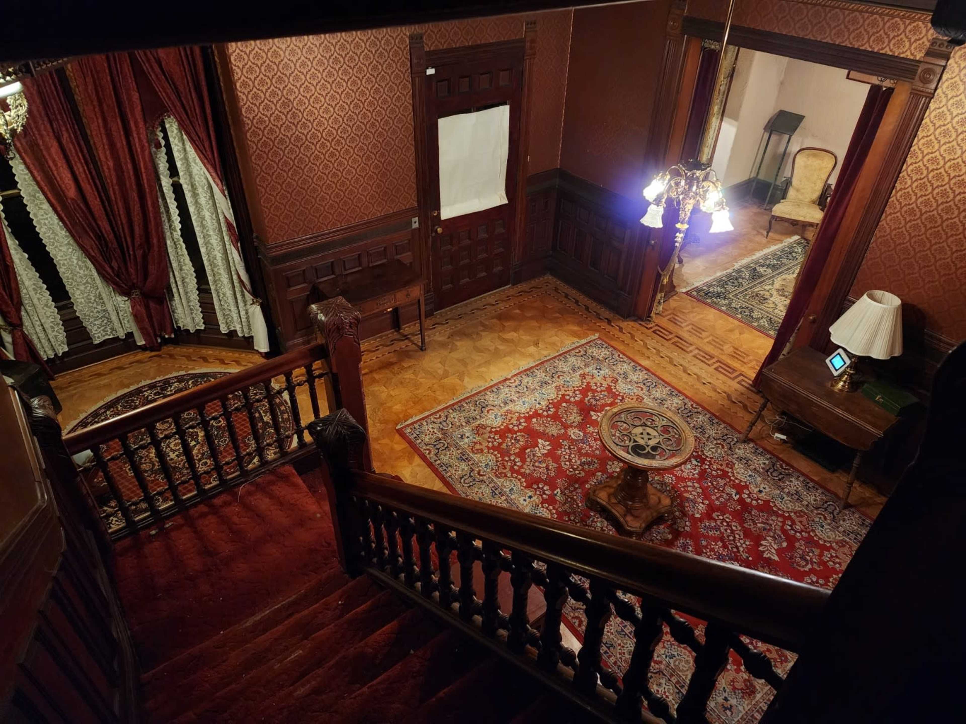 A staircase leading down to a richly decorated foyer with patterned wallpaper, ornate furniture, and a chandelier.