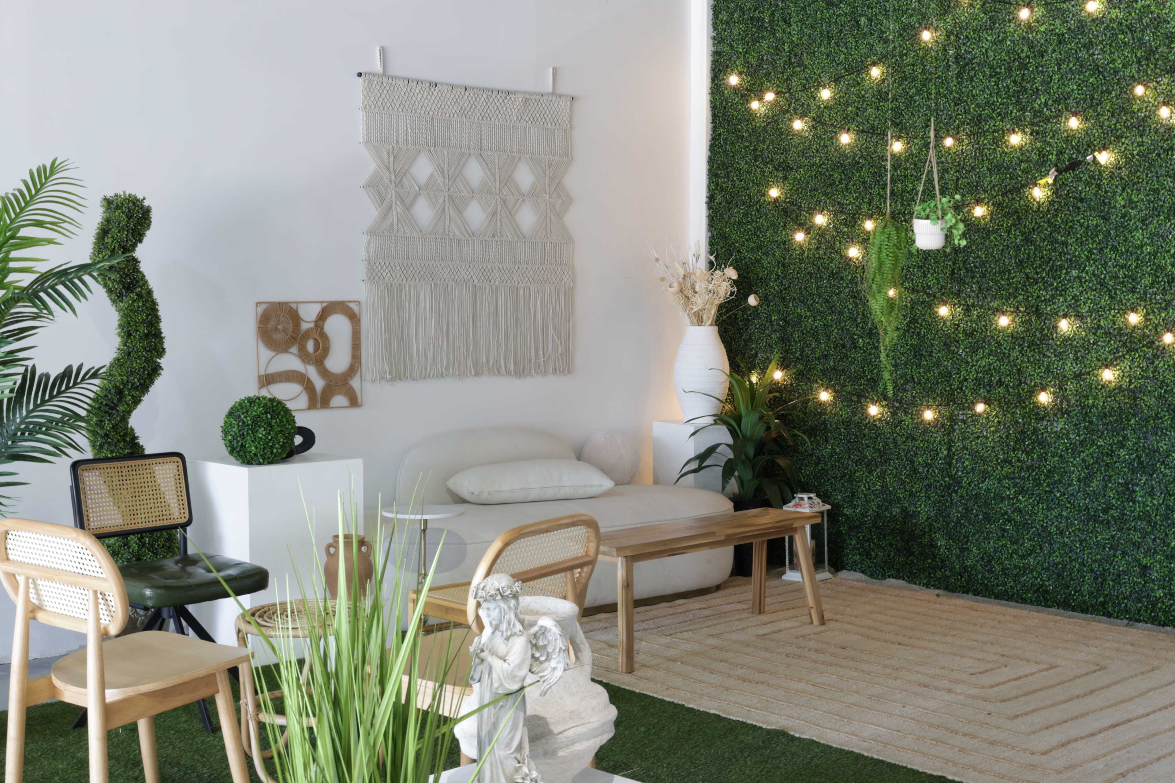 The scene features a cozy indoor space with a green wall of plants, a white sofa, wooden furniture, decorative items, and string lights.