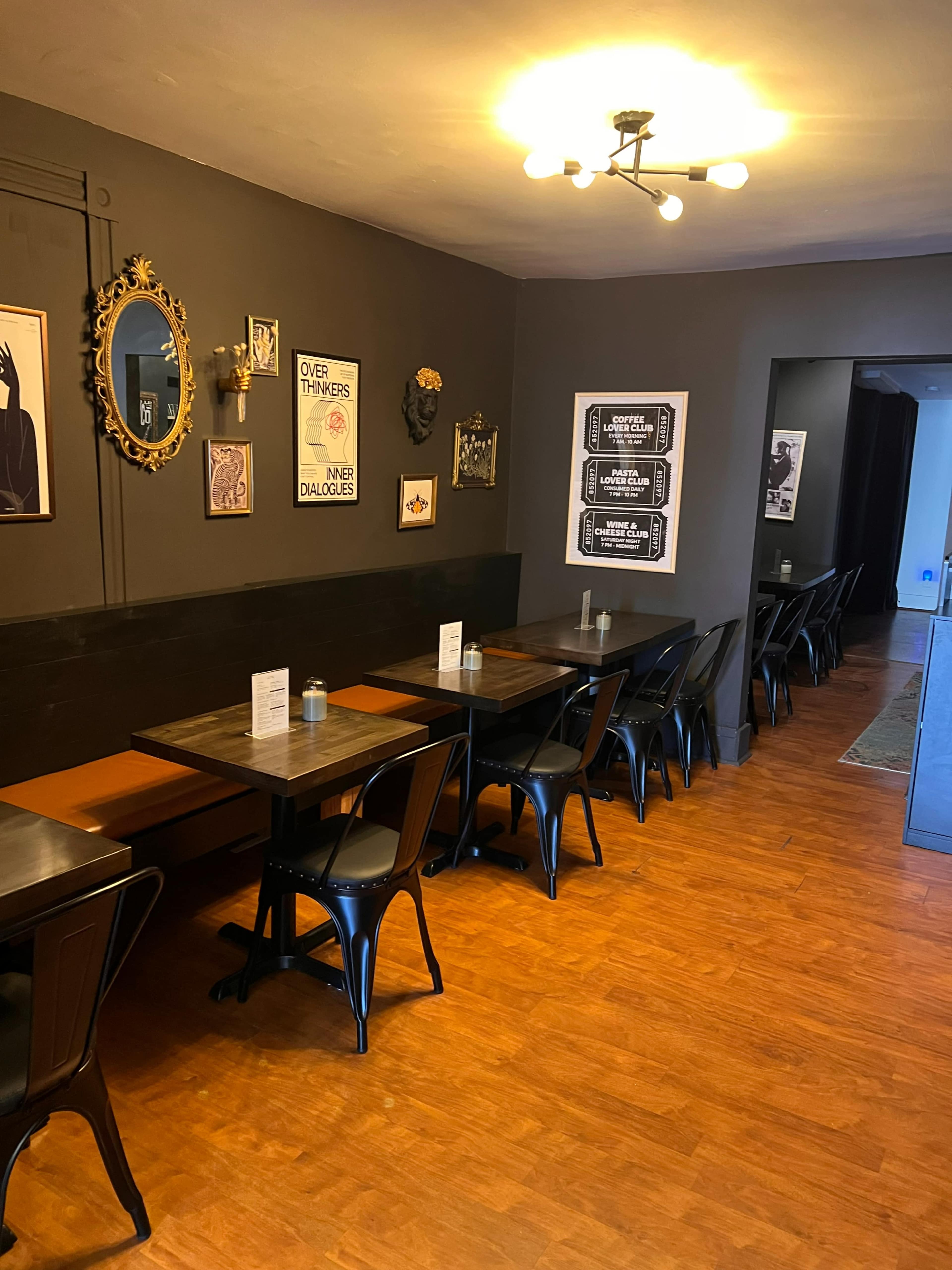 The image shows a cozy restaurant interior featuring wooden tables, metal chairs, and framed artwork on the walls.
