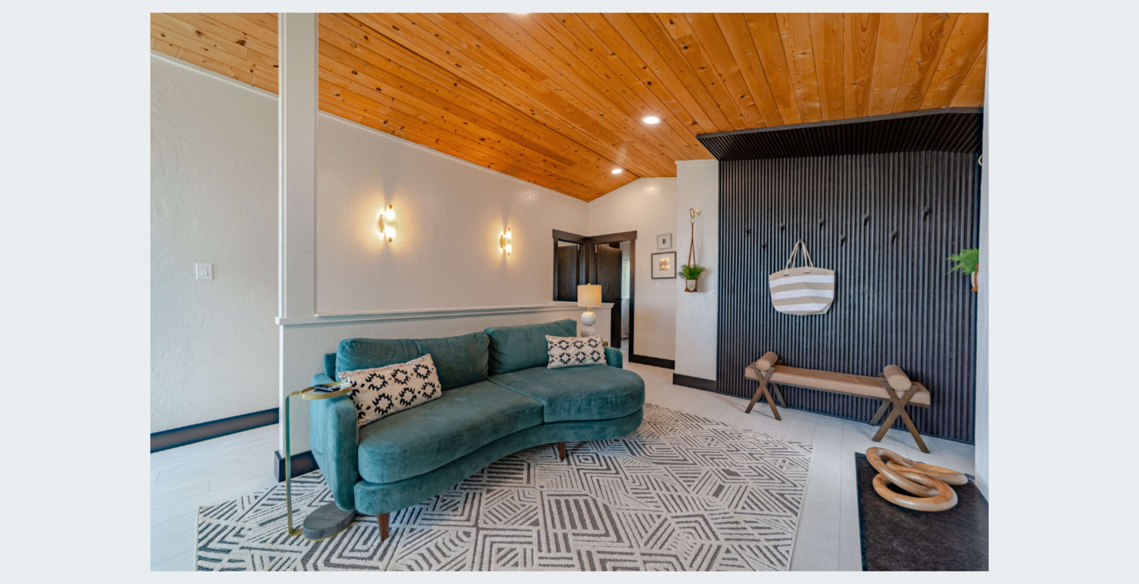 The image shows a modern living space with a teal curved sofa, a geometric area rug, and a dark accent wall featuring decorative hanging elements.