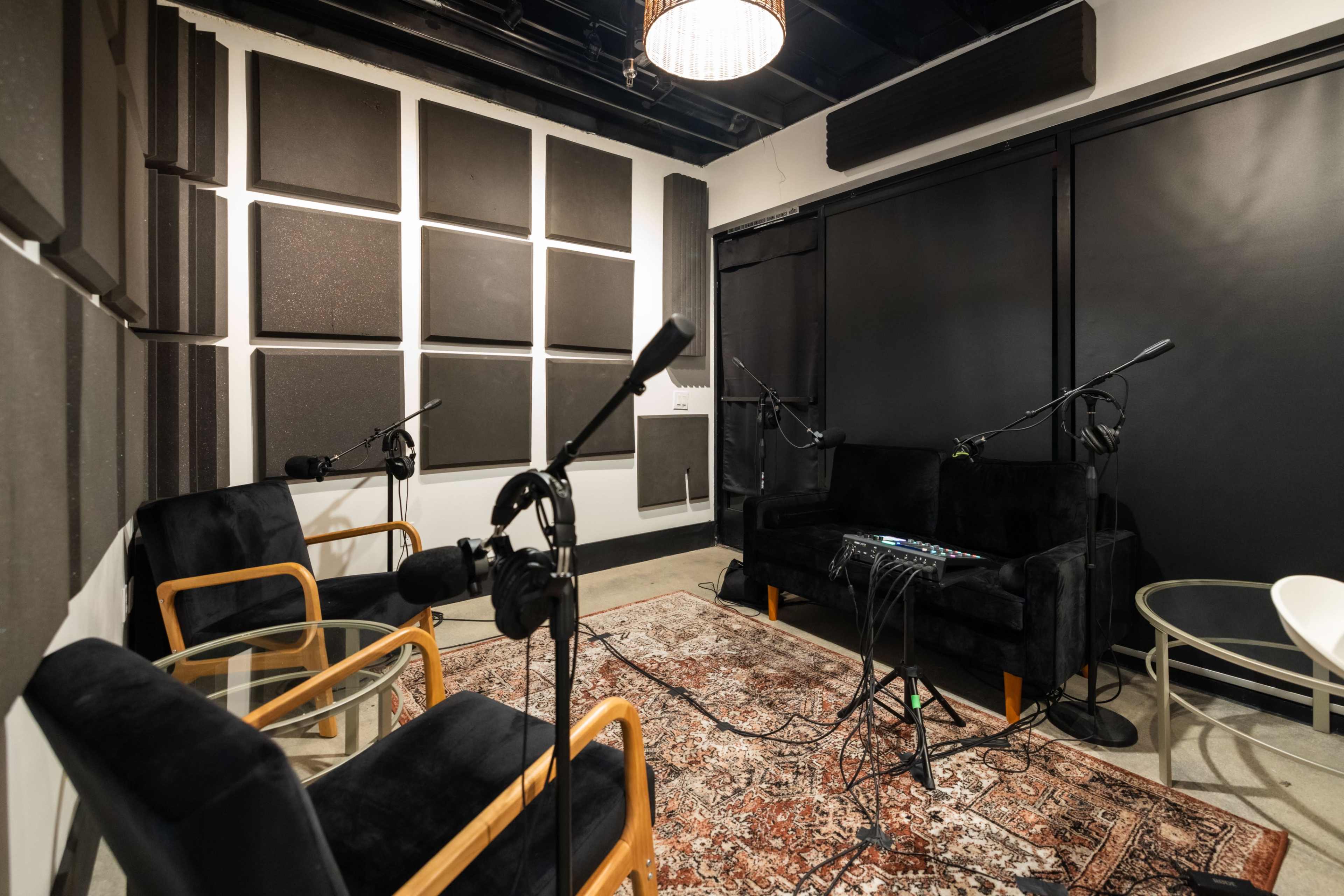 A soundproof recording studio with black walls, a patterned rug, and microphones positioned around a small seating area.