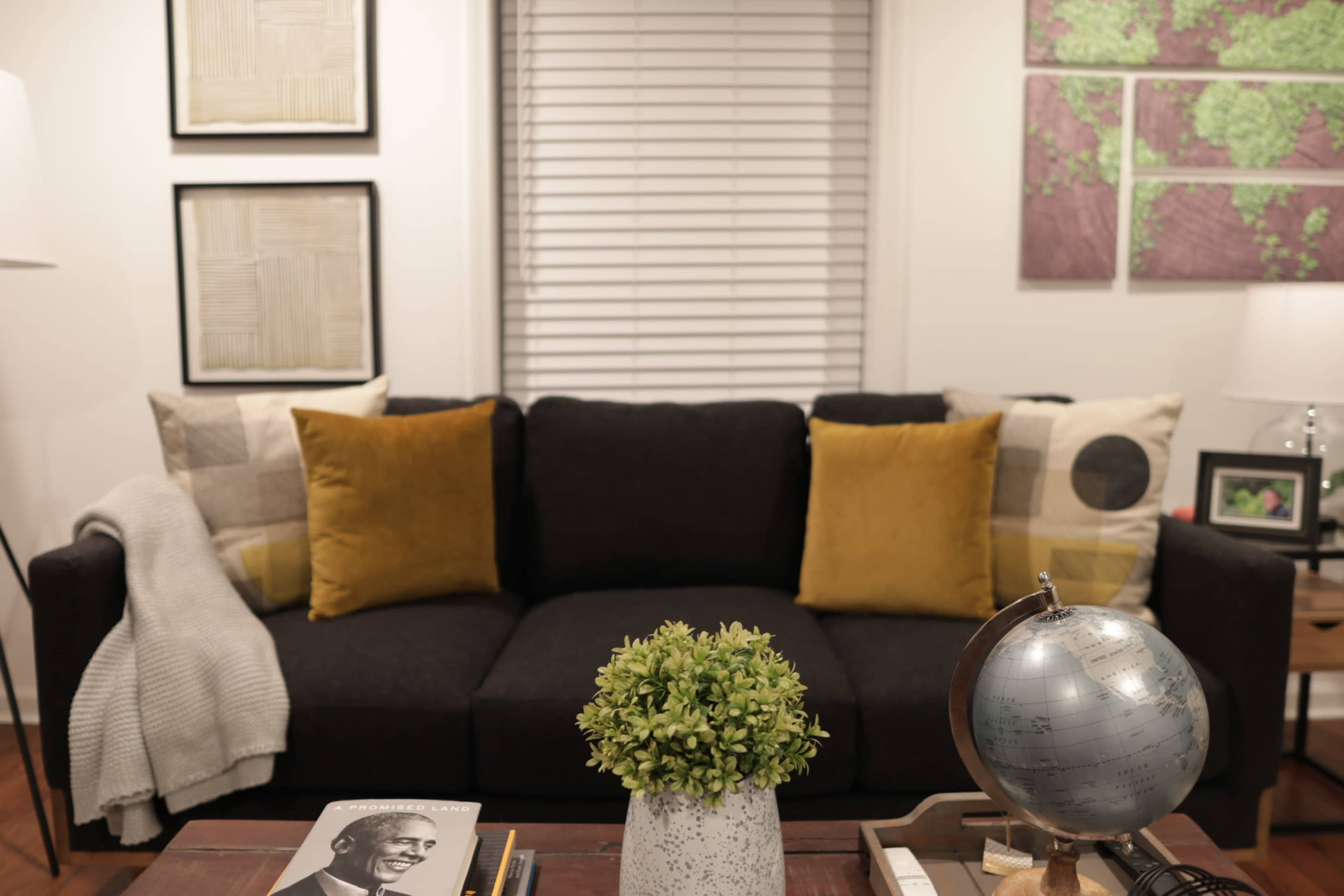 A dark sofa with yellow cushions is positioned in a well-lit room, accompanied by a decorative plant and a globe on a wooden table.