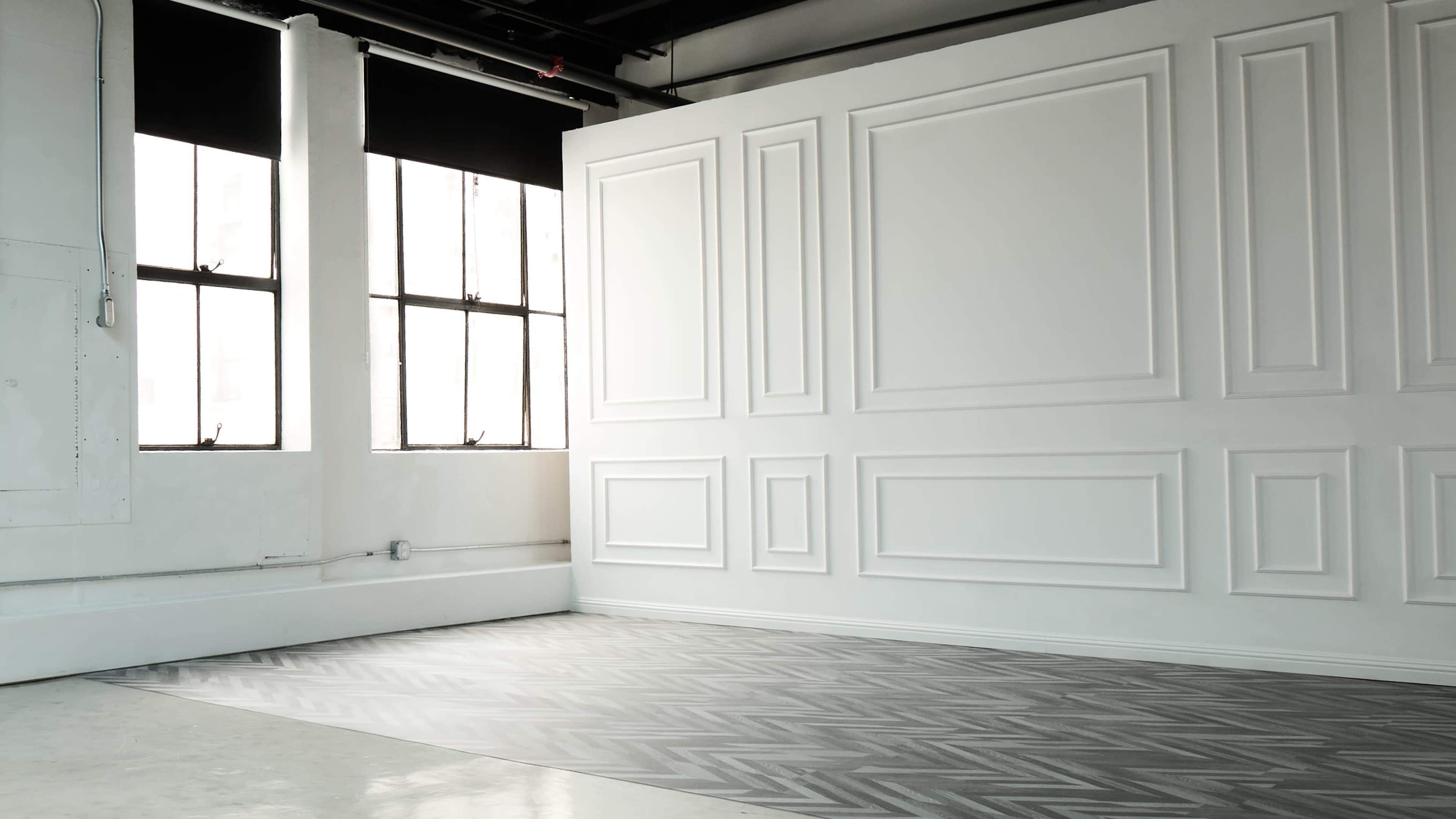 A brightly lit room with two large windows and a textured wall featuring rectangular paneling.