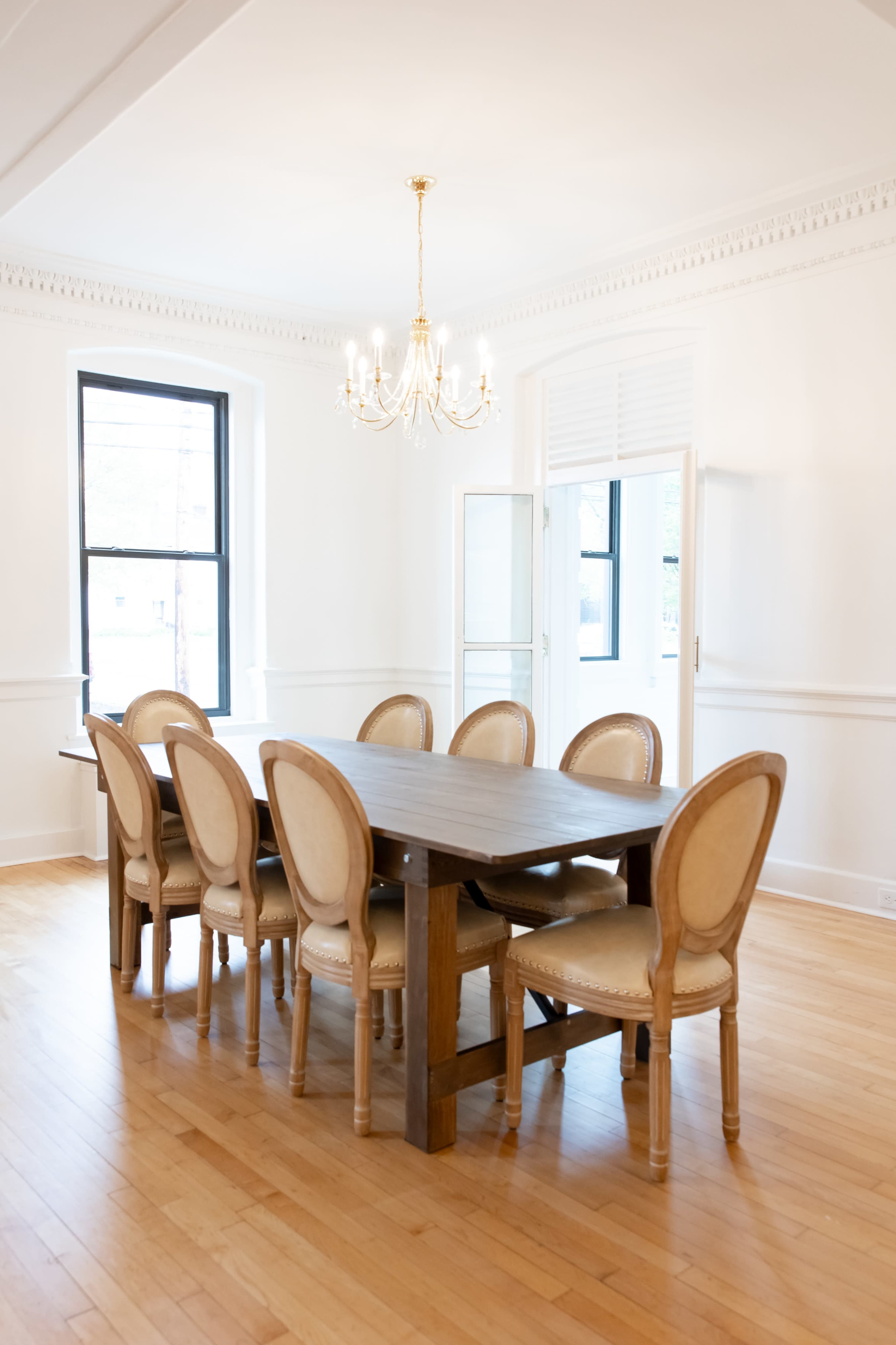 A spacious dining room features a wooden table surrounded by eight upholstered chairs, illuminated by a chandelier.