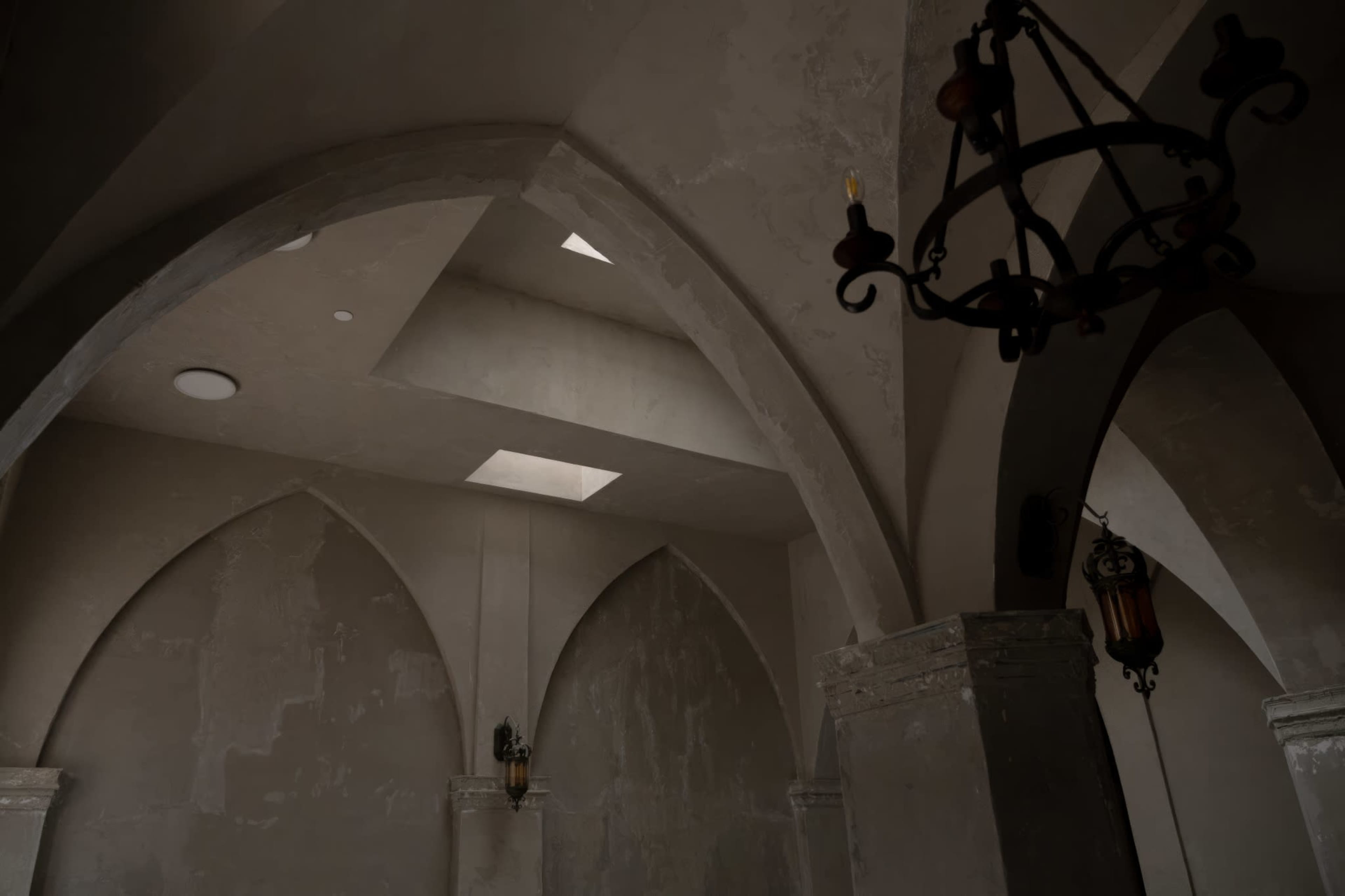 The image depicts a room with high arched ceilings, stone columns, and light fixtures hanging from the ceiling.