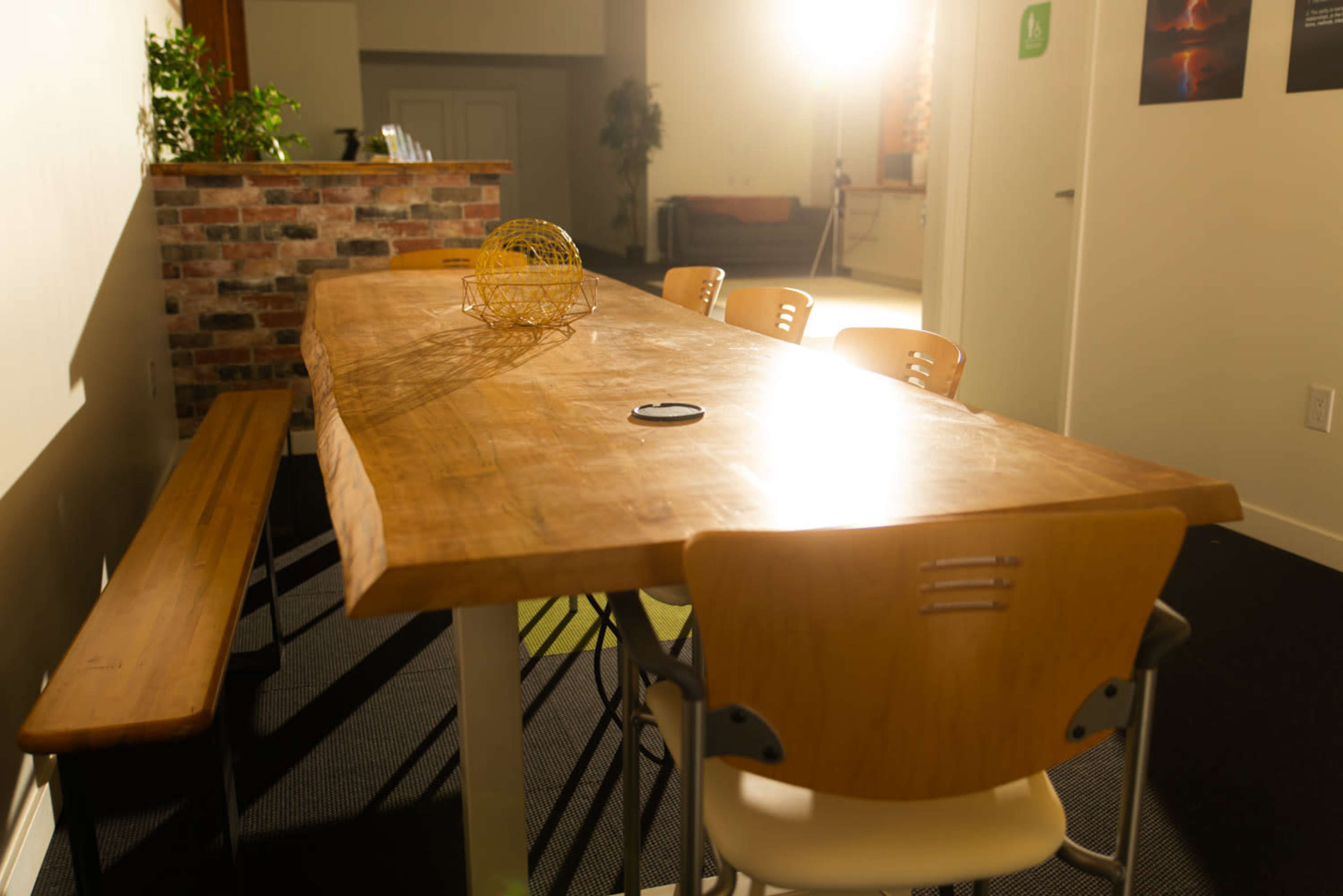 A wooden table with a geometric centerpiece is placed beside a long bench in a well-lit room.