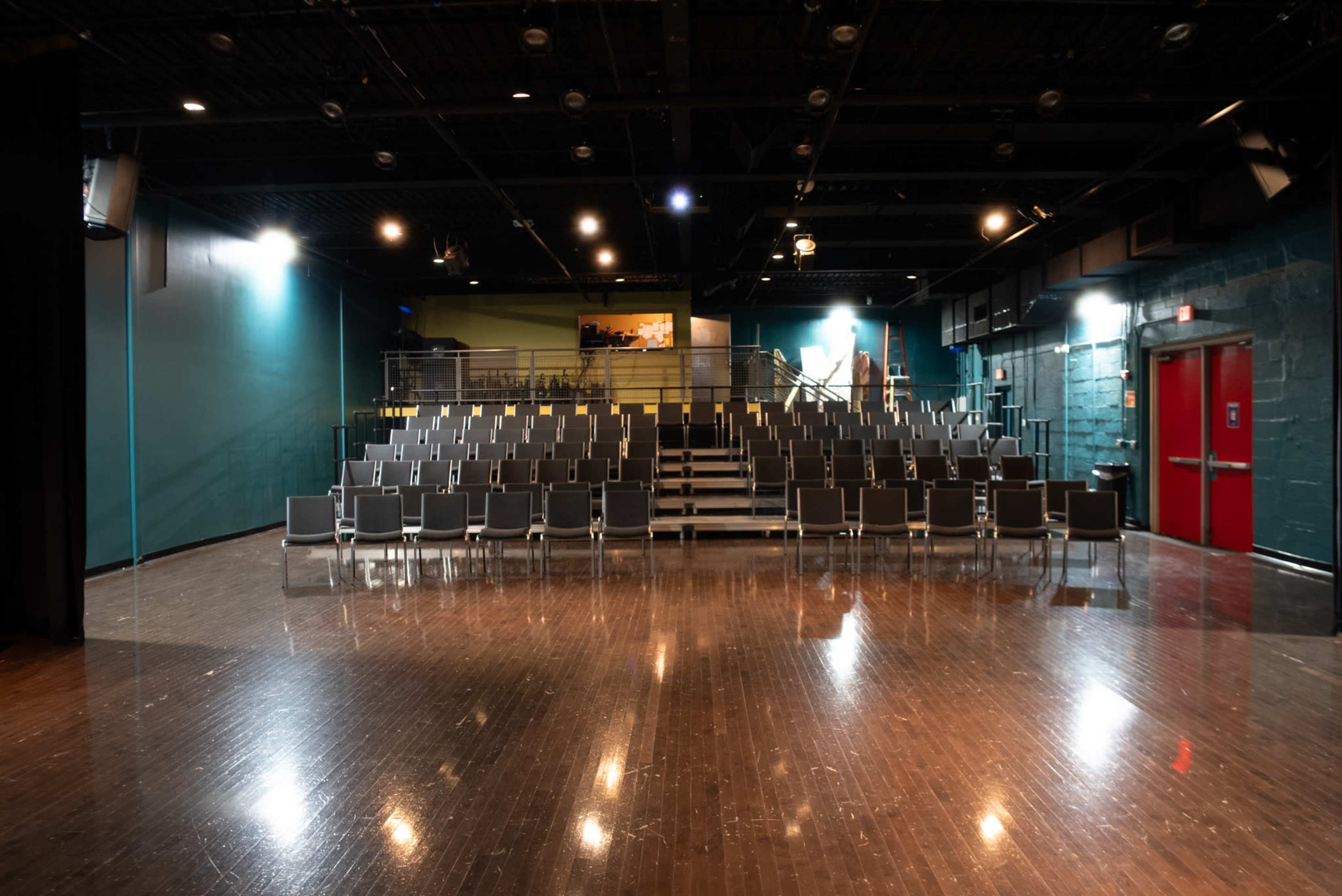 A small theater space with rows of black chairs facing a stage and a shiny wooden floor.