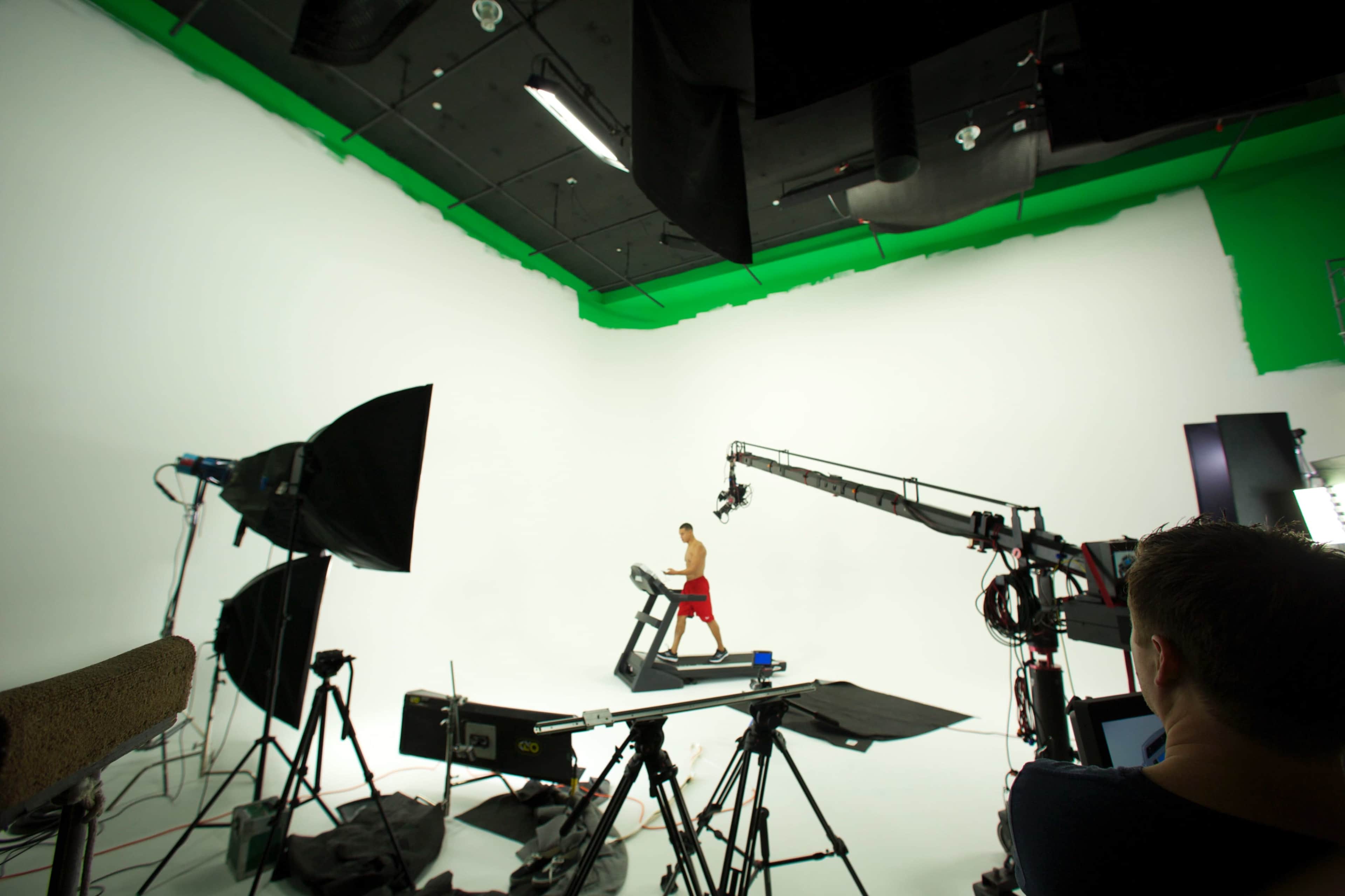 A person runs on a treadmill in a studio surrounded by professional lighting and filming equipment.