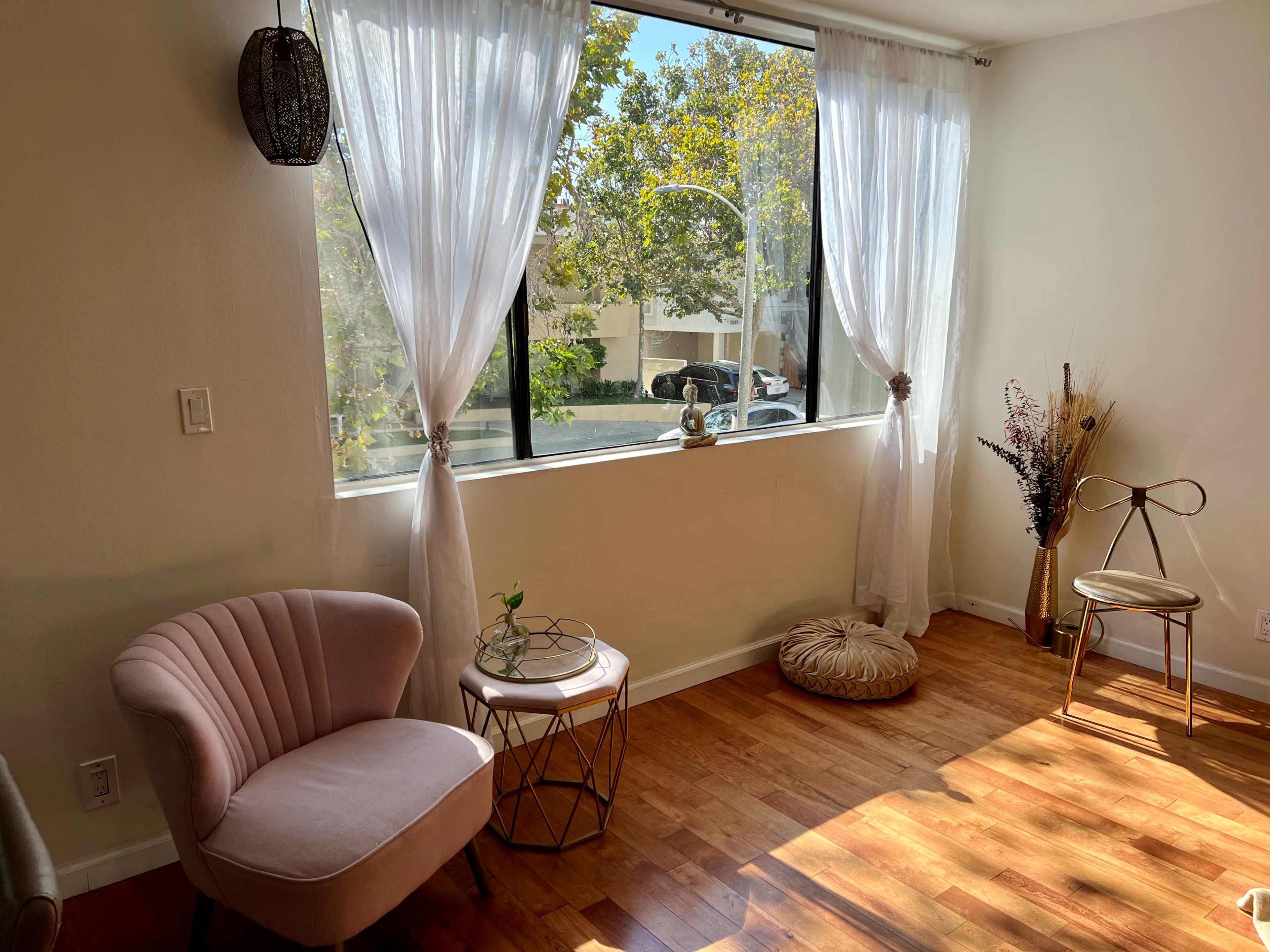 A well-lit room with large windows, a pair of chairs, a small table, and decorative plants.