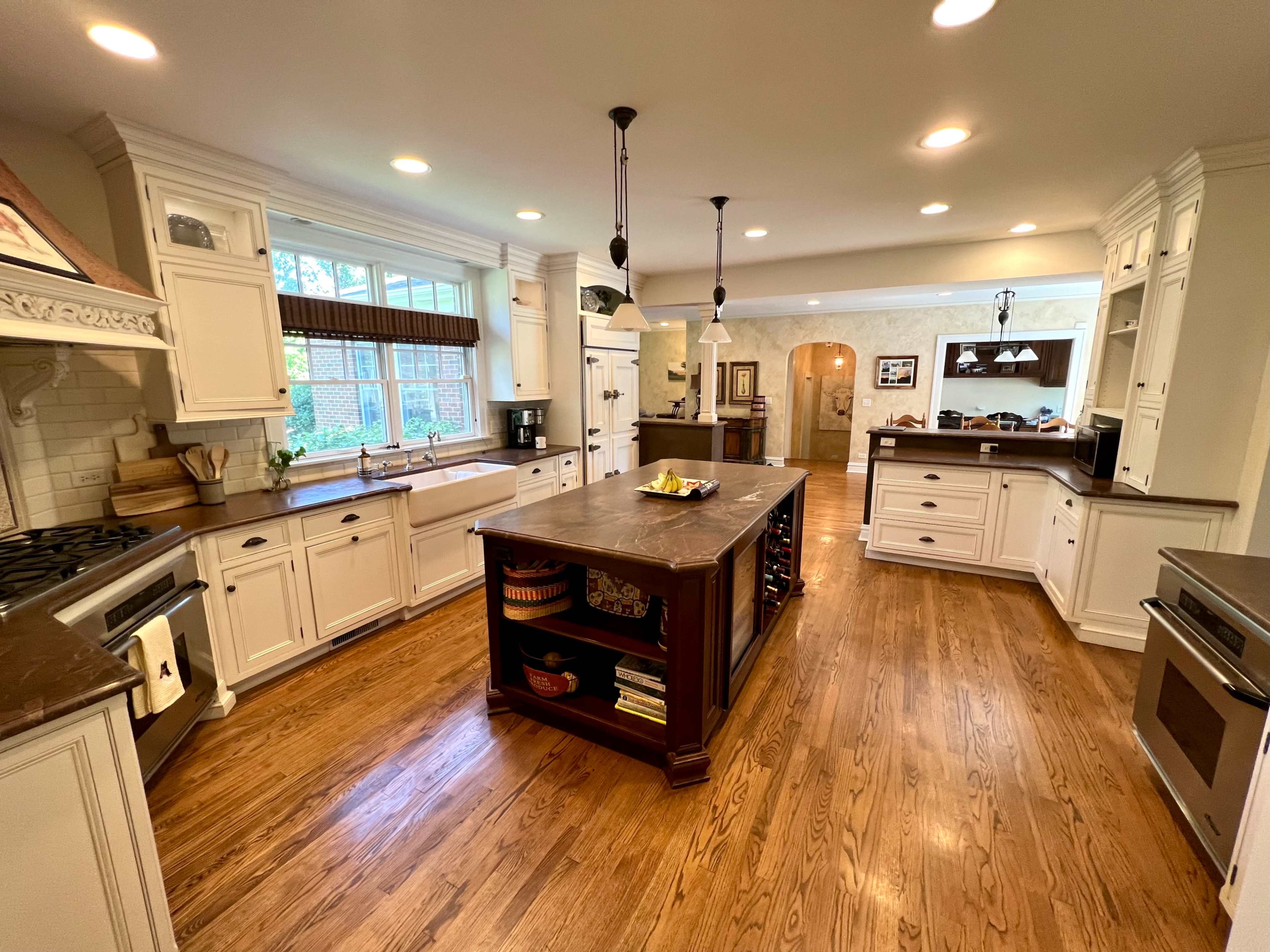 A spacious kitchen features white cabinetry, a central island with a dark countertop, and hardwood floors.