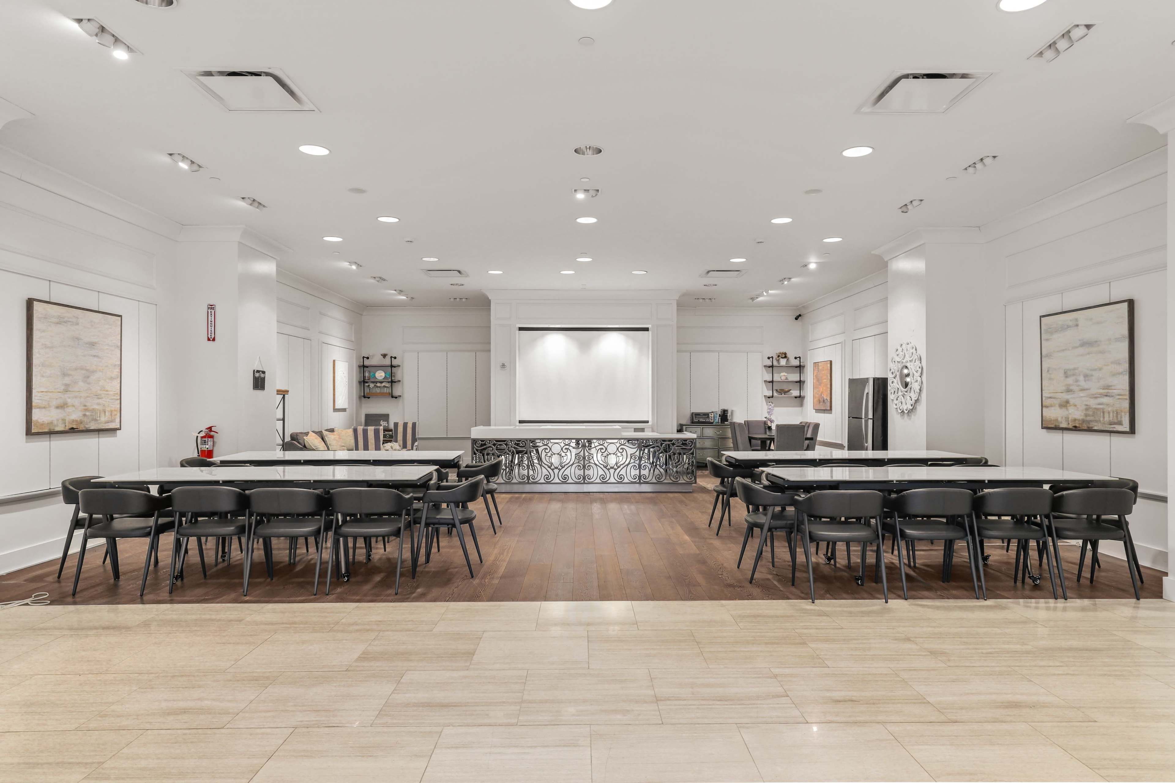 The image shows a spacious, well-lit meeting room with multiple rectangular tables arranged in a U-shape and an area for presentations at the front.