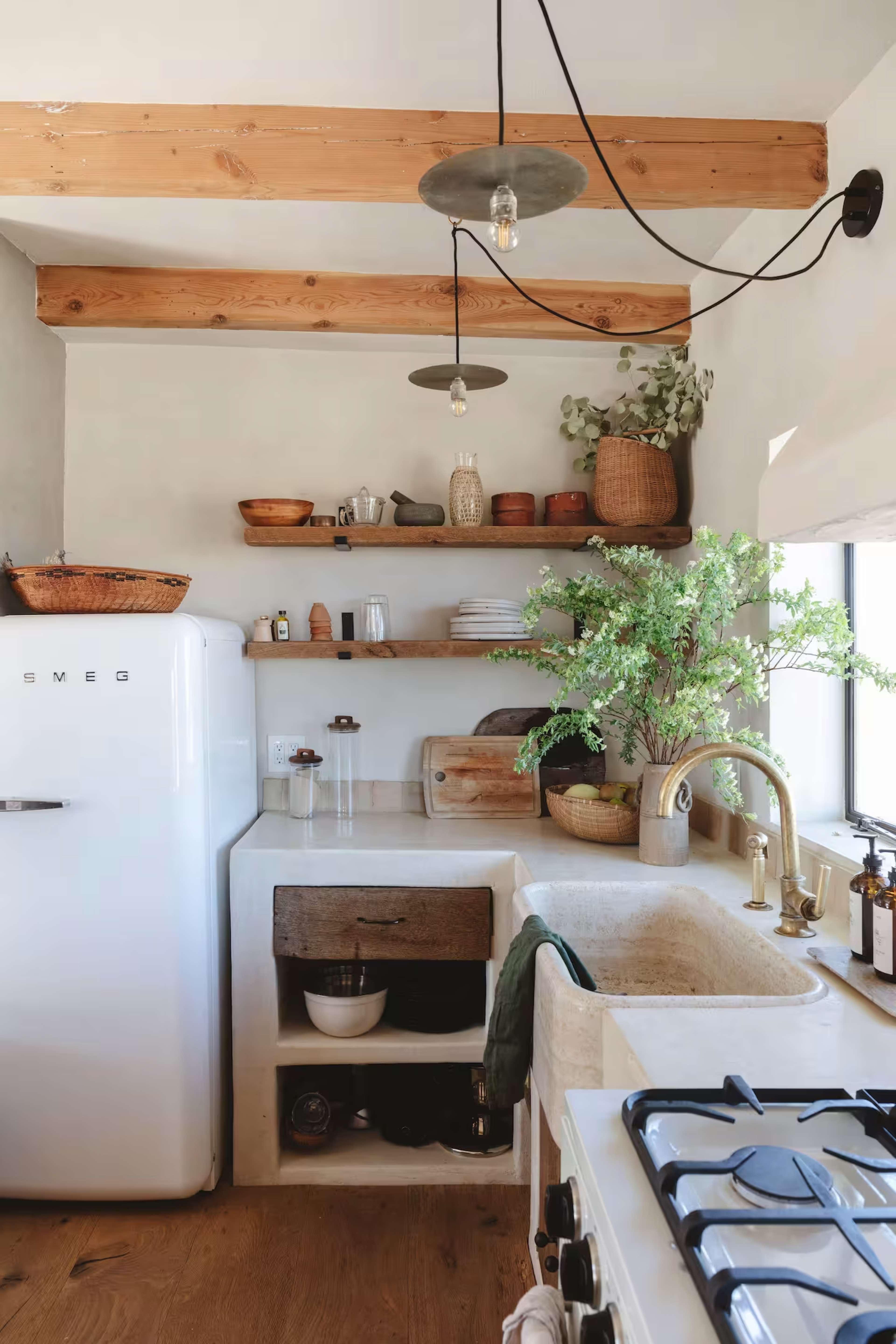 A modern kitchen features wooden beams, open shelving with various containers, a Smeg refrigerator, and a gas stove with a sink beside it.