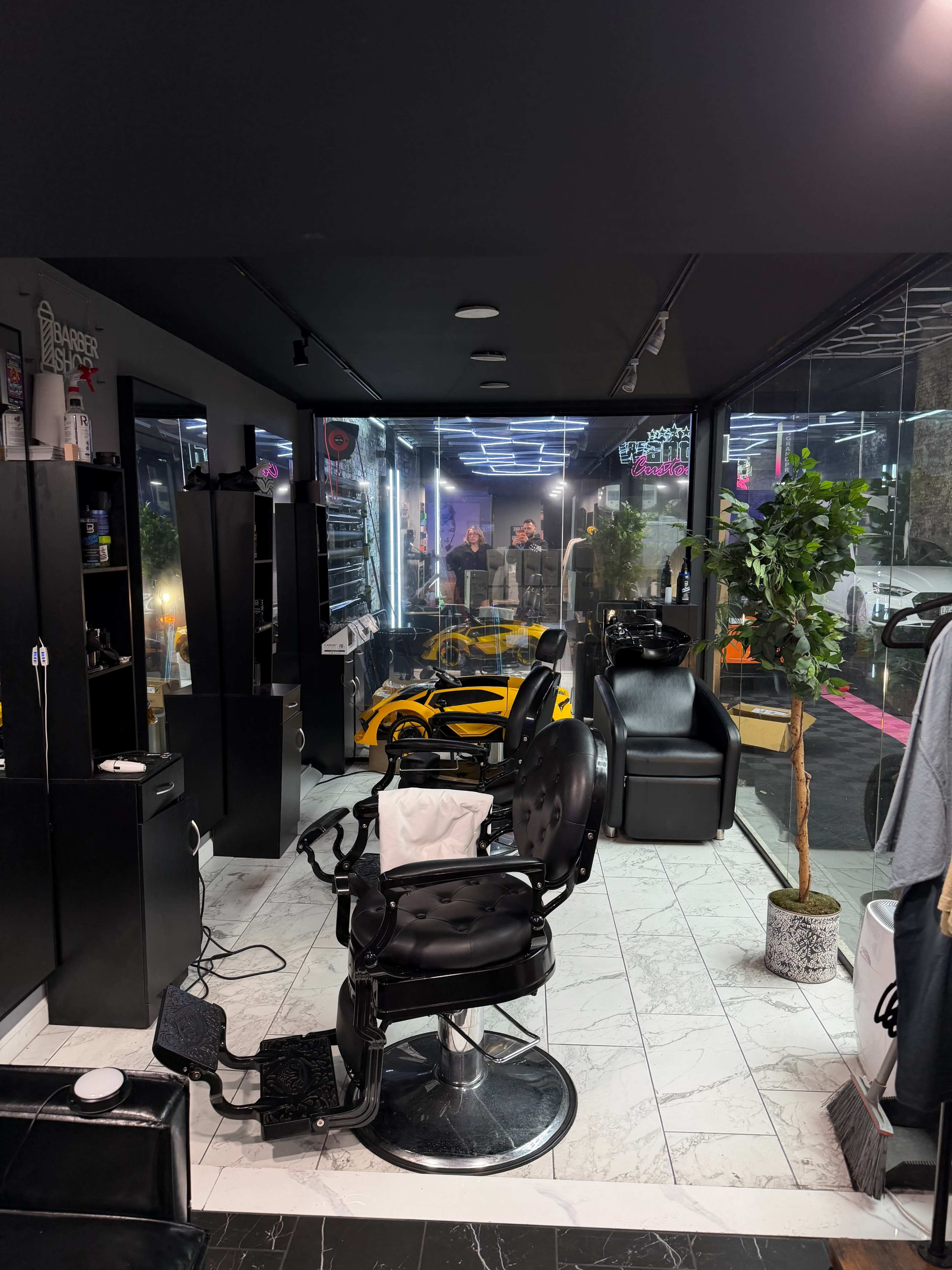 The image shows a modern hair salon featuring black styling chairs, a sleek design, and large glass windows displaying a view of the street outside.