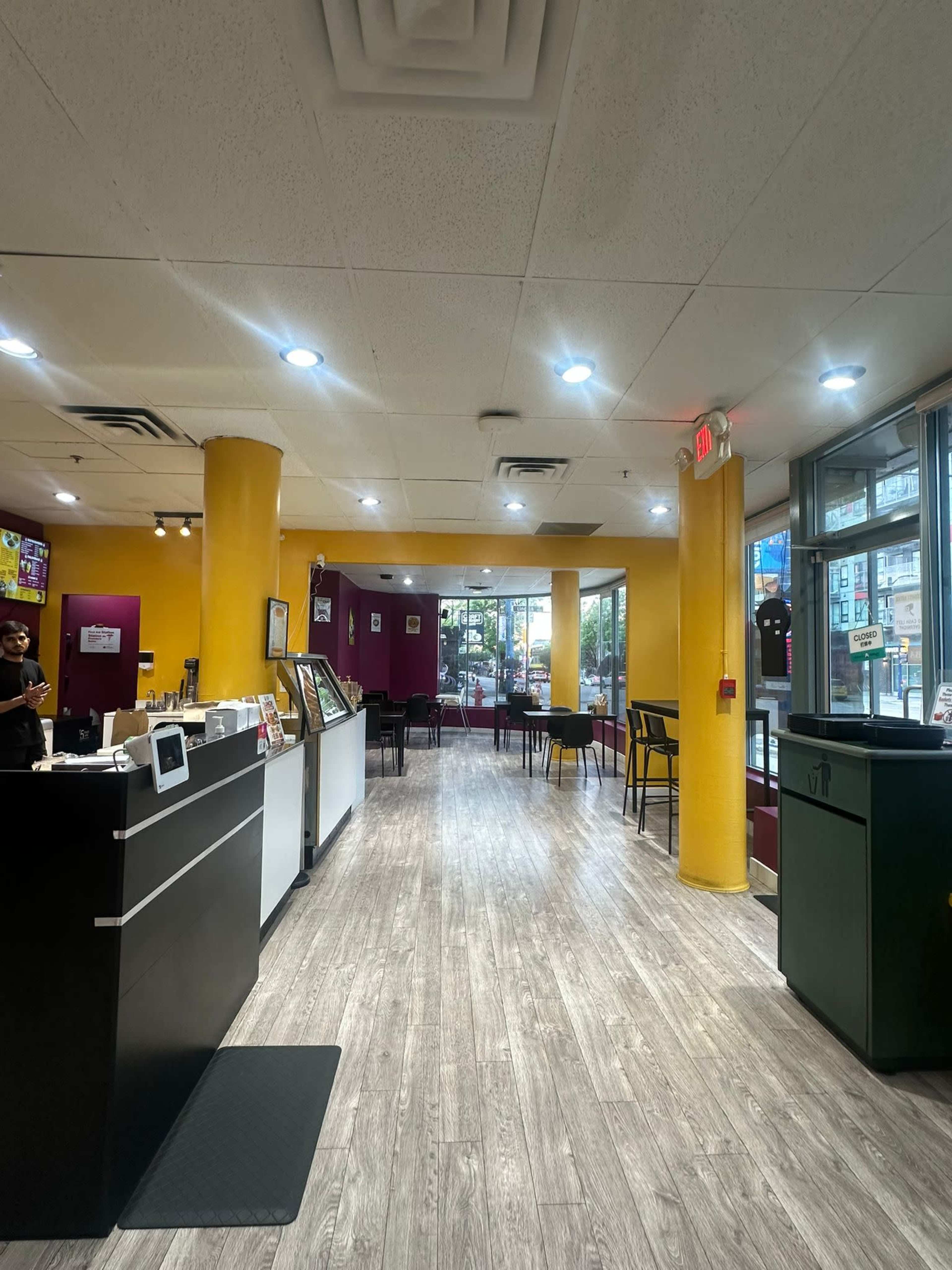 The image shows a brightly lit café interior with a counter on the left and empty tables arranged throughout the space.