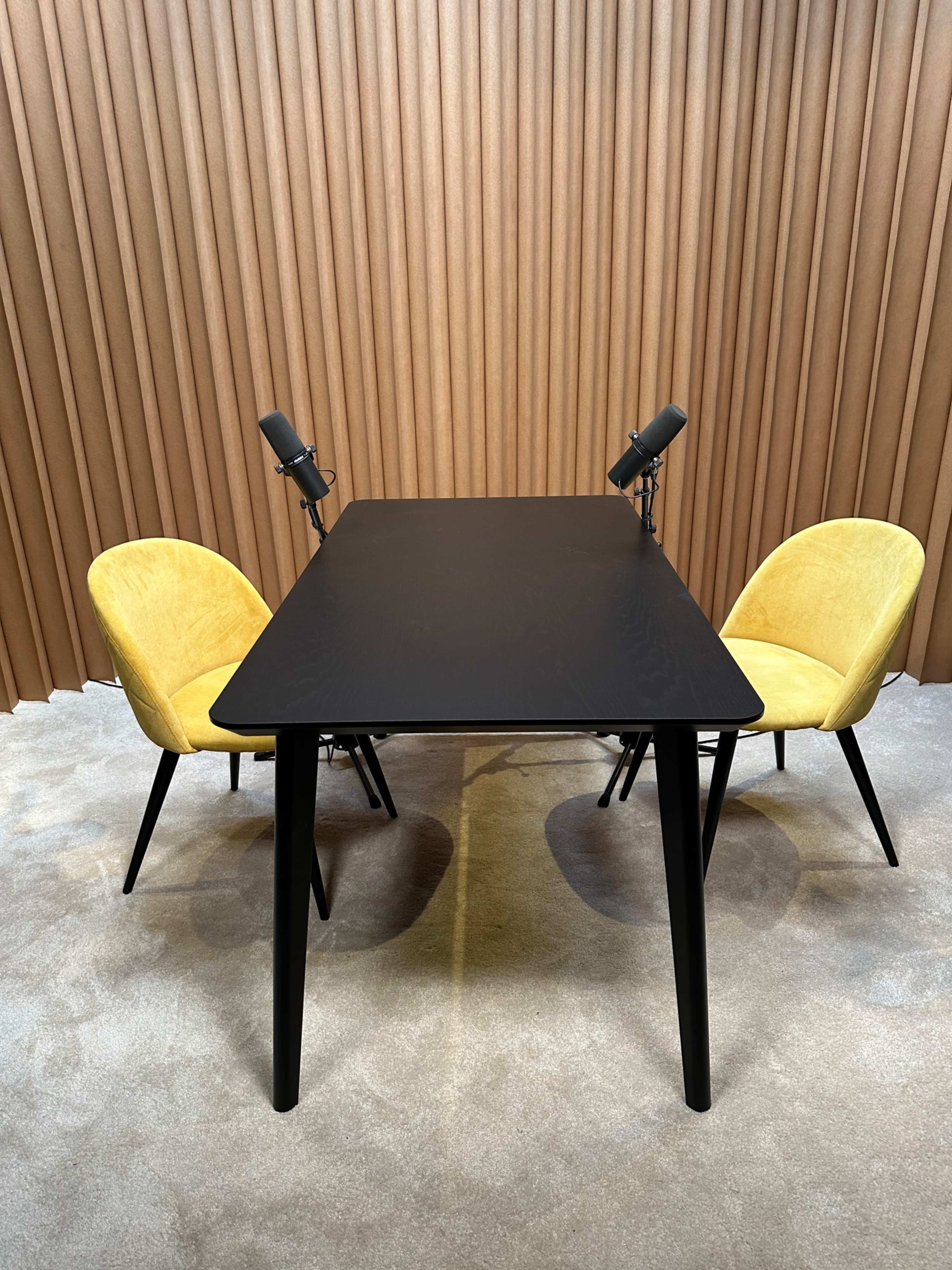 A black table with two yellow chairs sits on a carpeted floor in front of a textured brown backdrop.