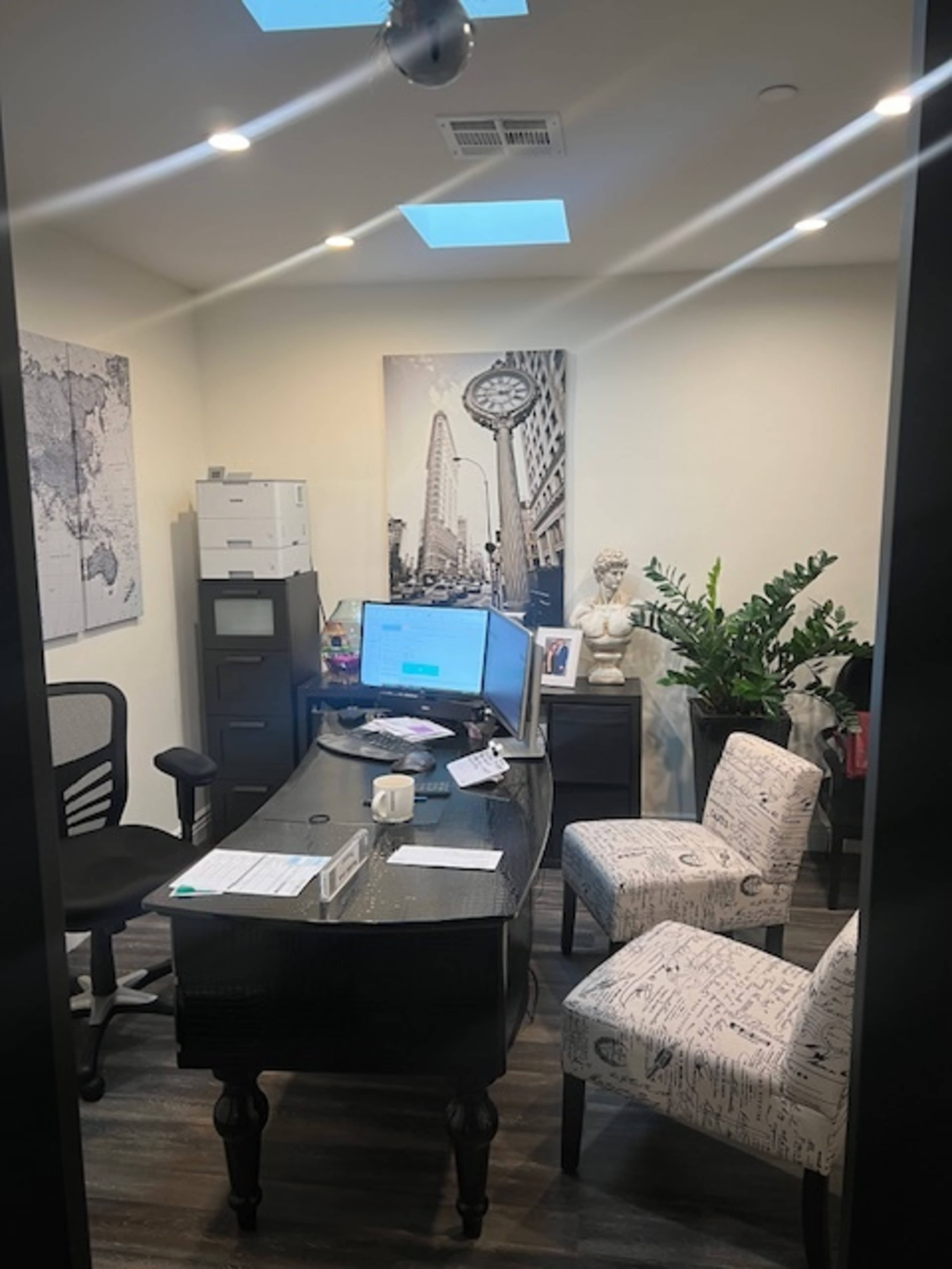 The image shows a small office space with a desk, two chairs, a printer, and a large wall art depicting a cityscape.