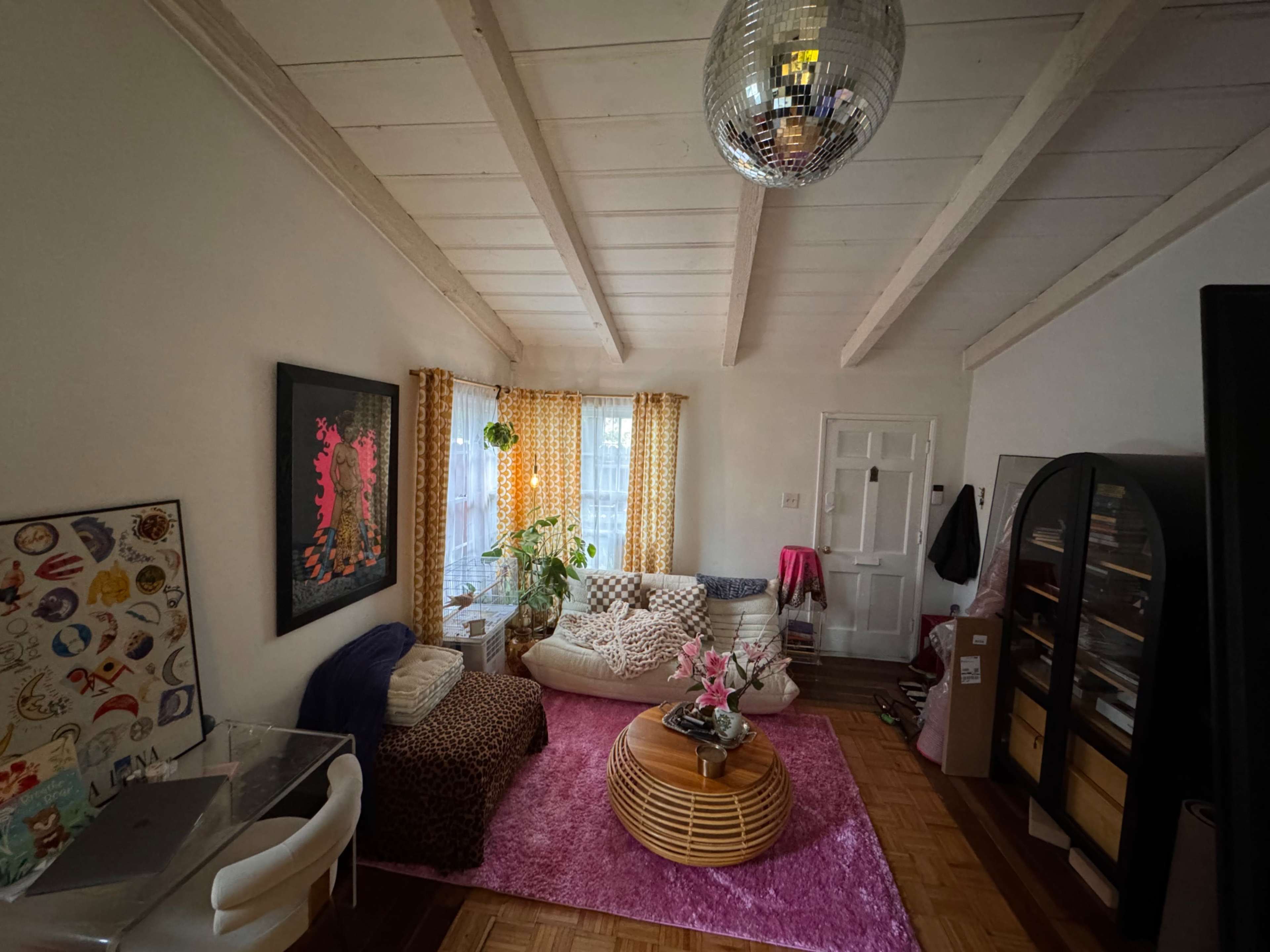 A cozy living room with a circular coffee table, a white sofa, patterned curtains, and a disco ball hanging from the ceiling.