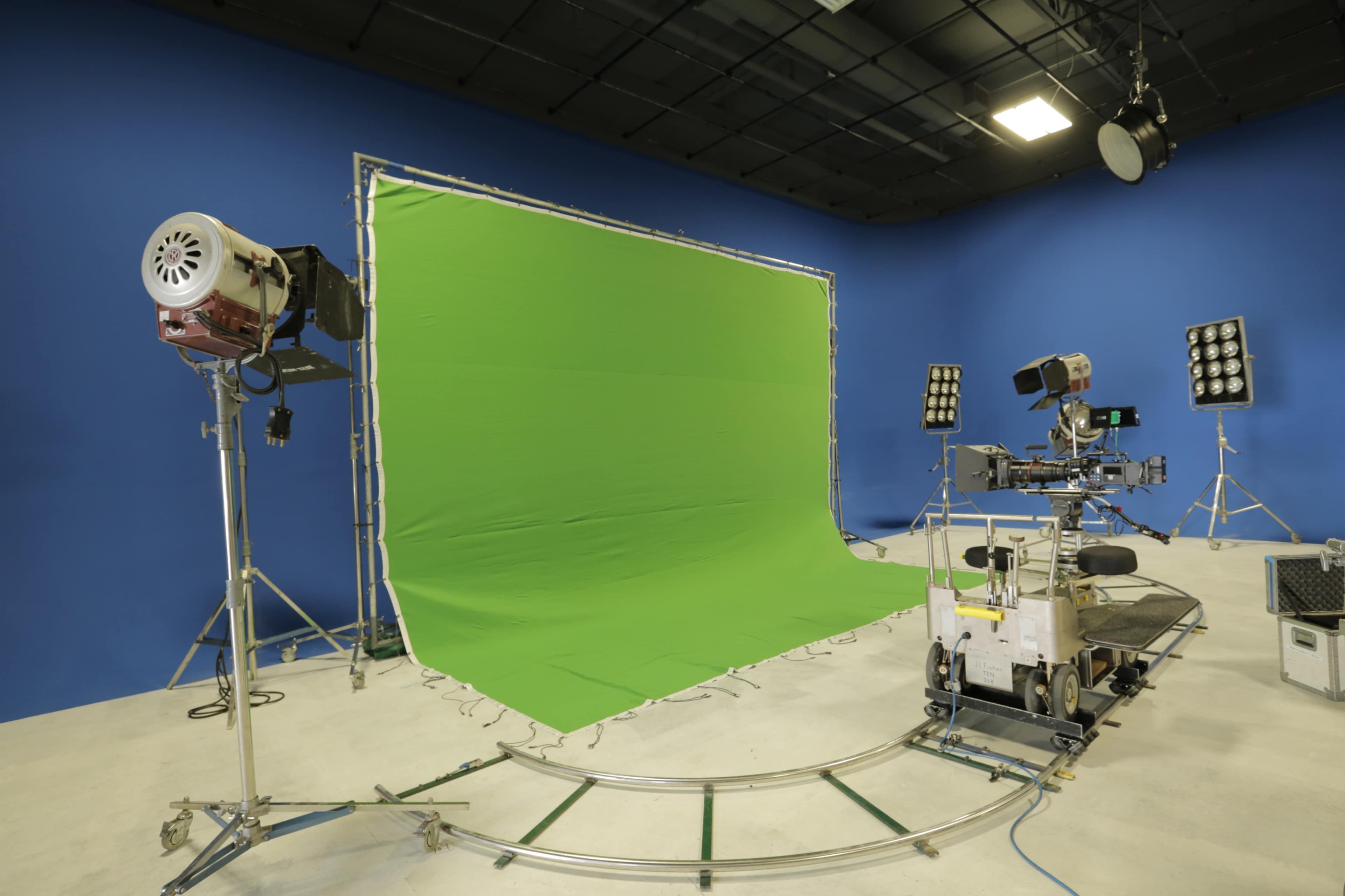 The image shows a film studio equipped with a green screen backdrop and various lighting and camera equipment set up for a production.