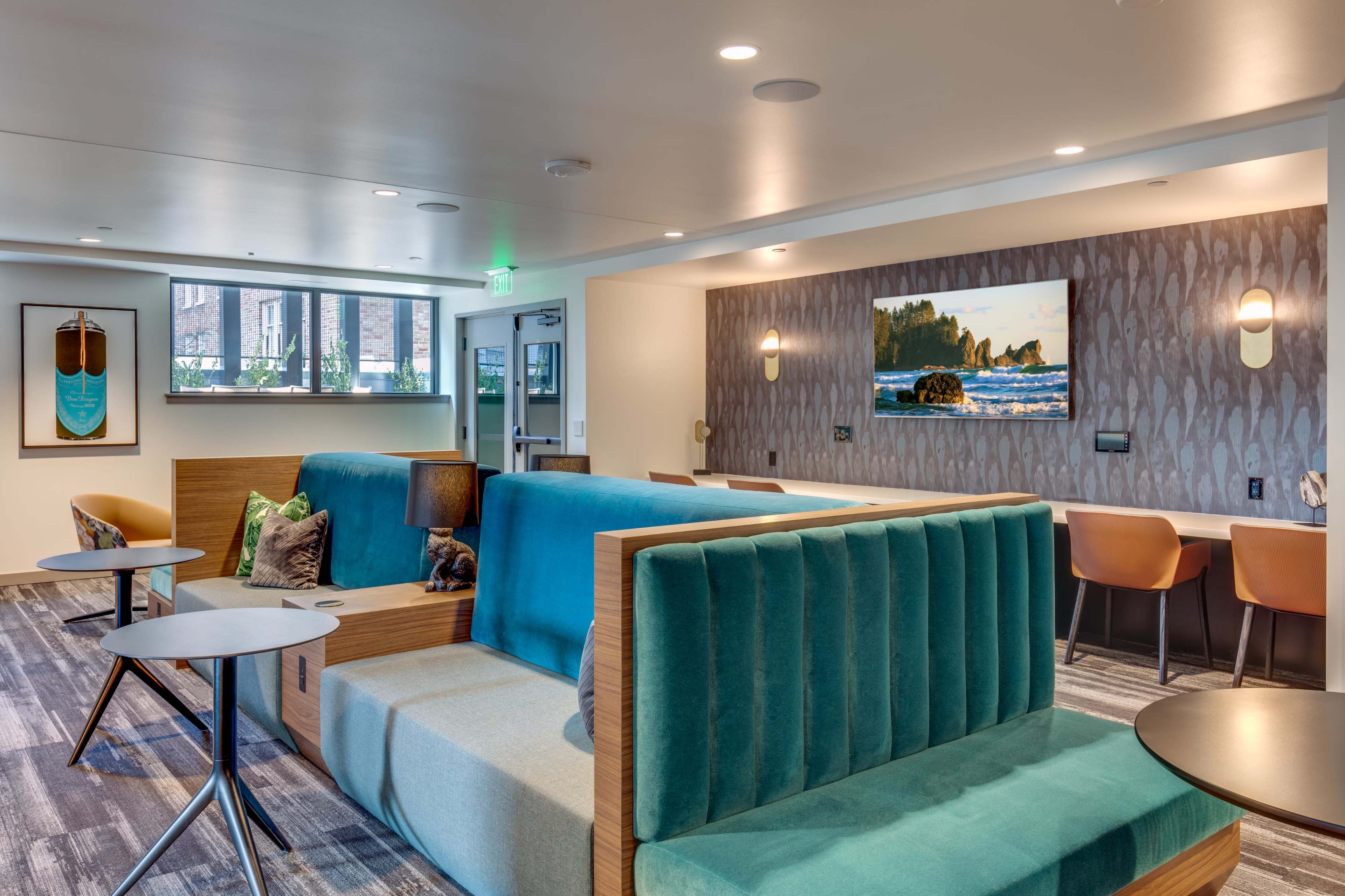 A modern lounge area features green upholstered seating, small tables, and a wall-mounted television.