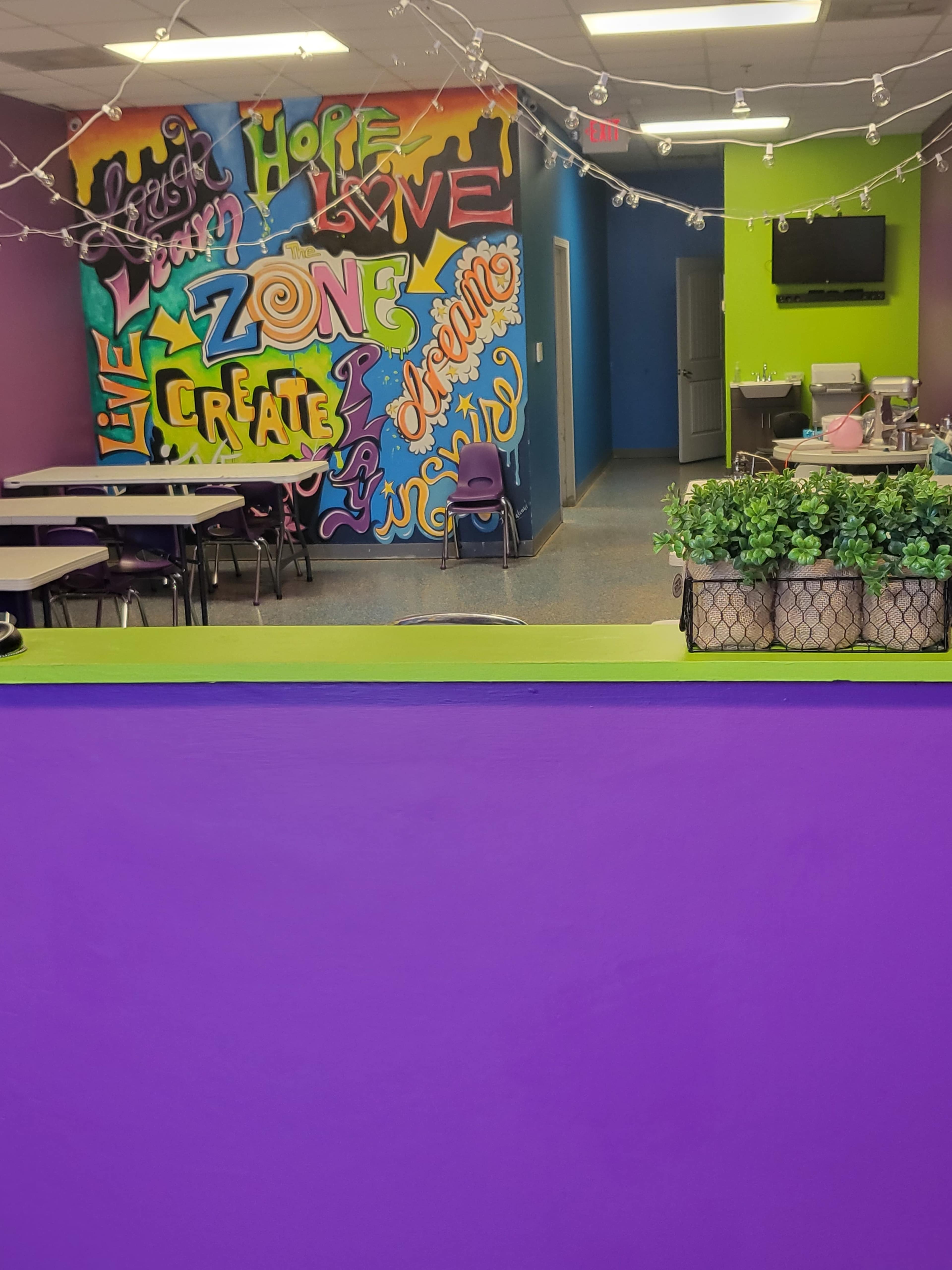 A brightly colored room featuring a wall with graffiti-style art, along with tables and chairs organized in a creative space.