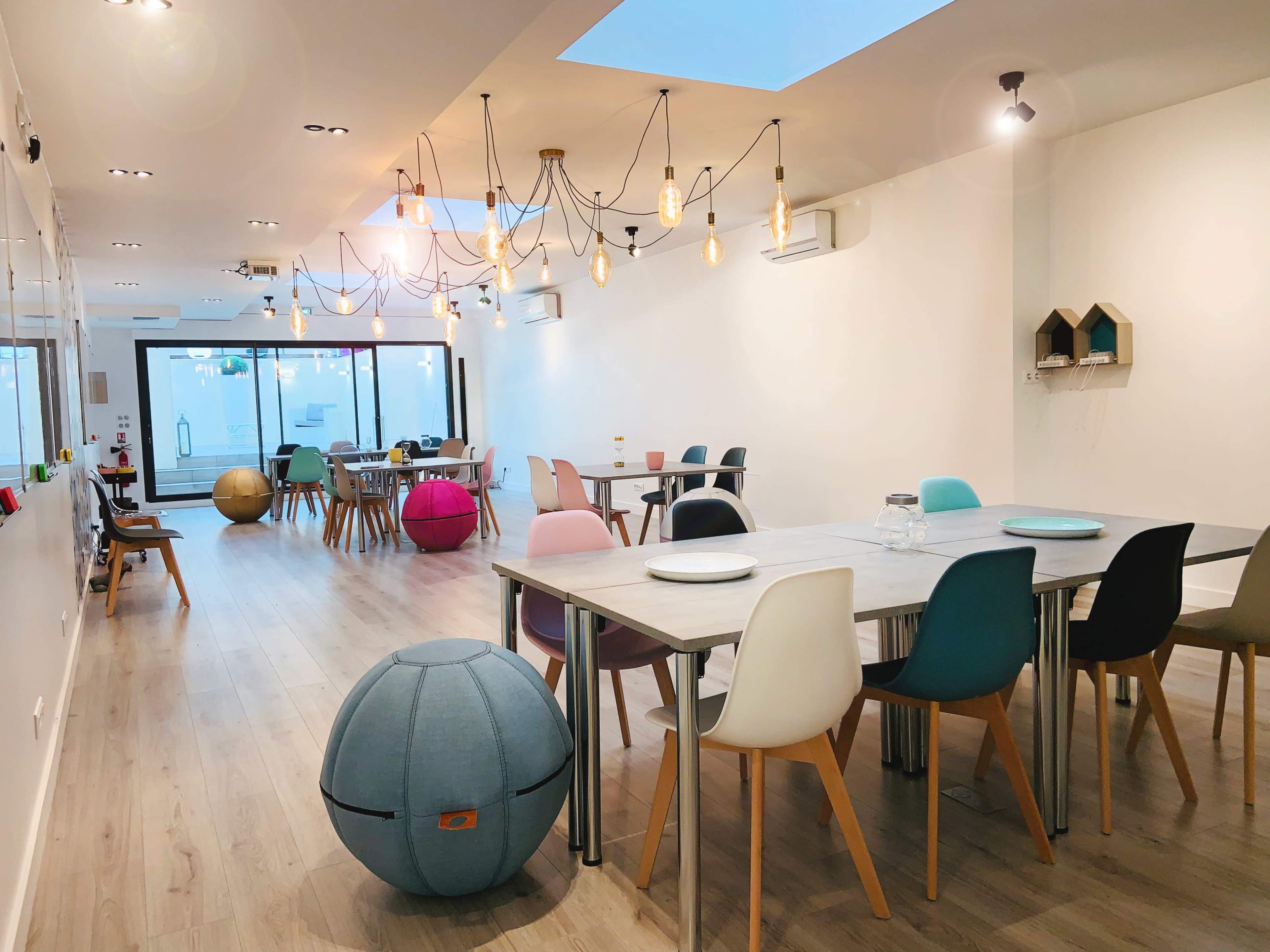 A modern cafe with a light-filled interior featuring various seating arrangements, including tables and colorful chairs.