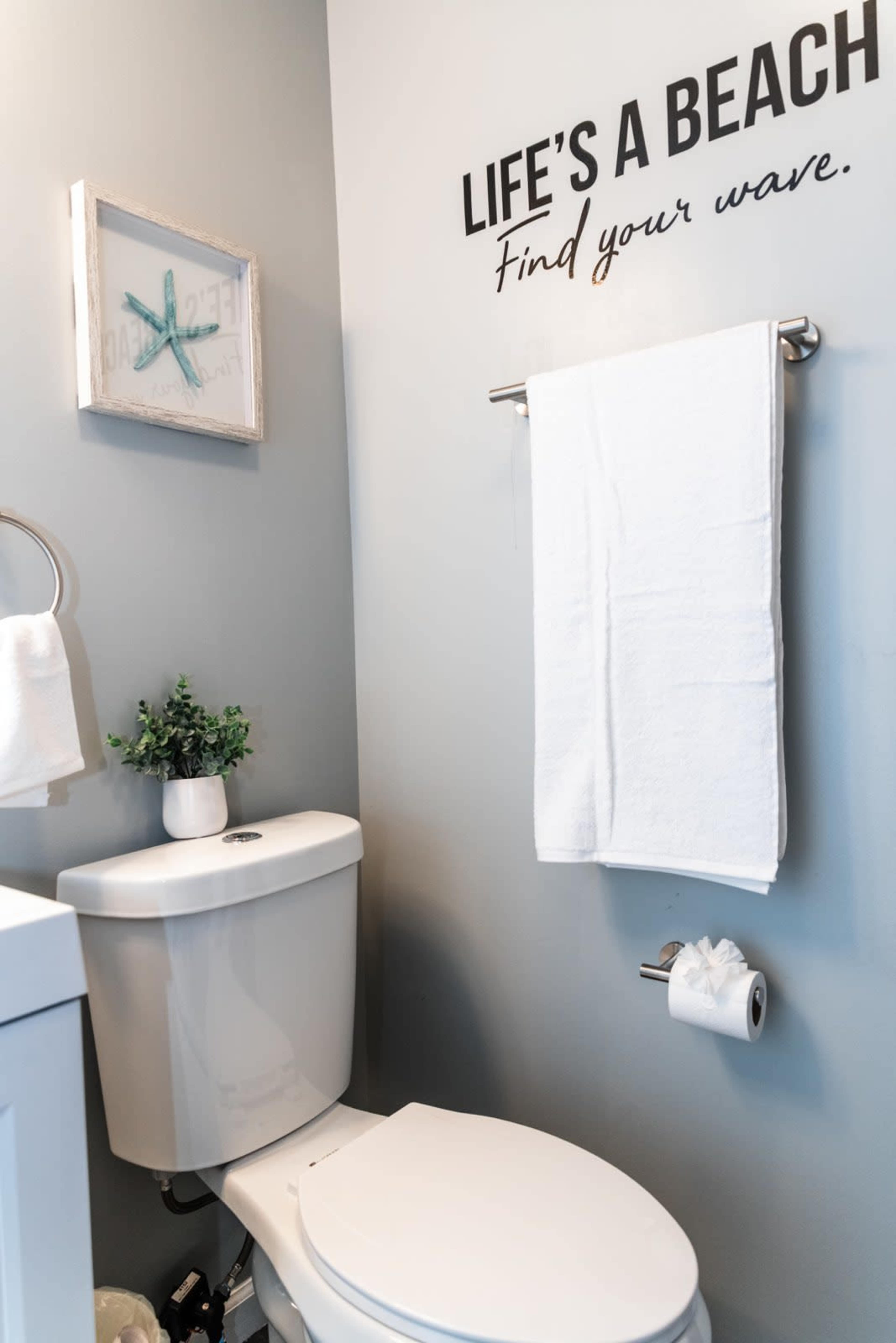 A bathroom features a toilet beside a wall adorned with a decorative sign and a framed starfish picture.