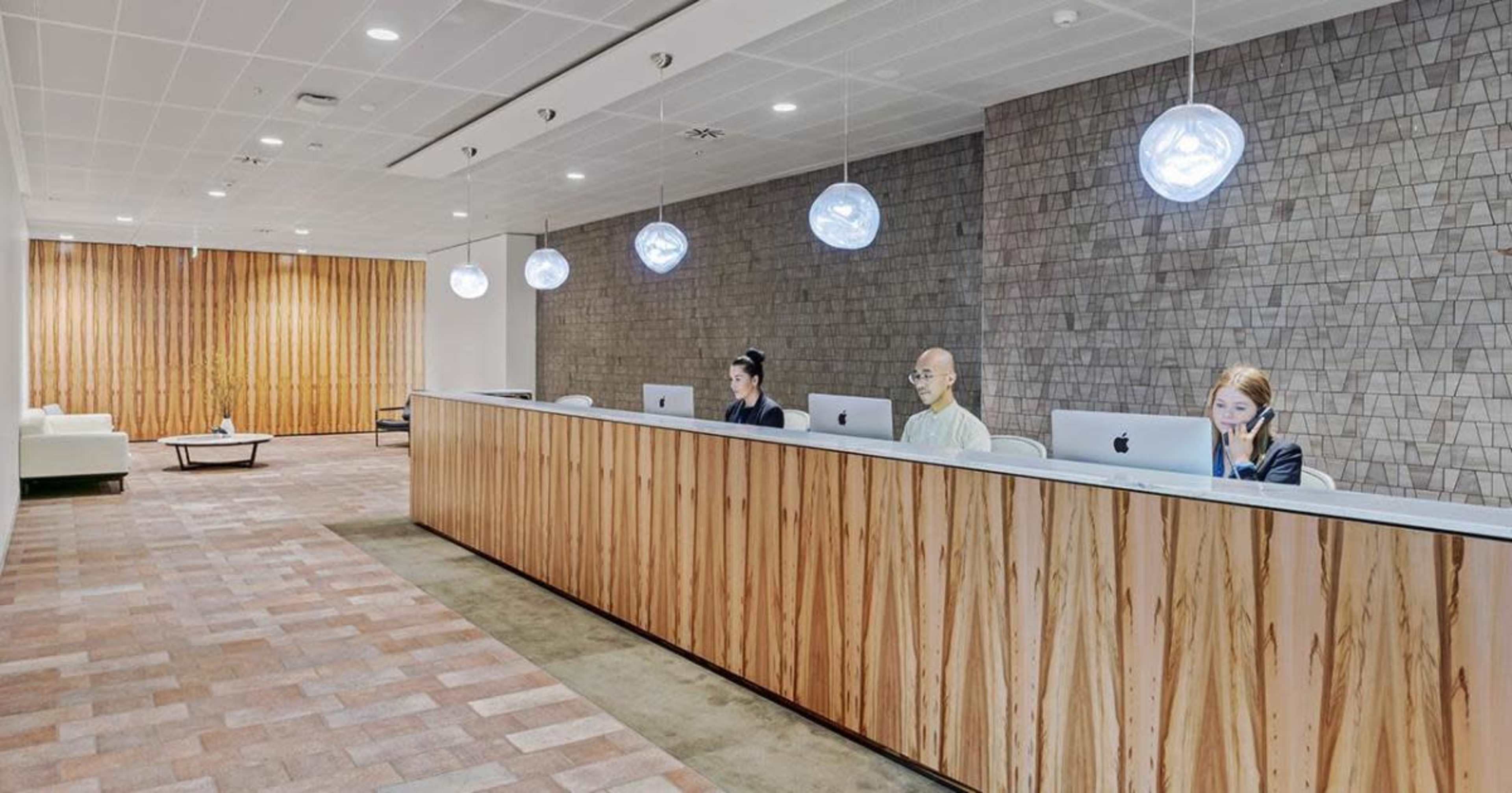 A reception area features a long wooden desk with three employees working on iMacs beneath modern pendant lights.