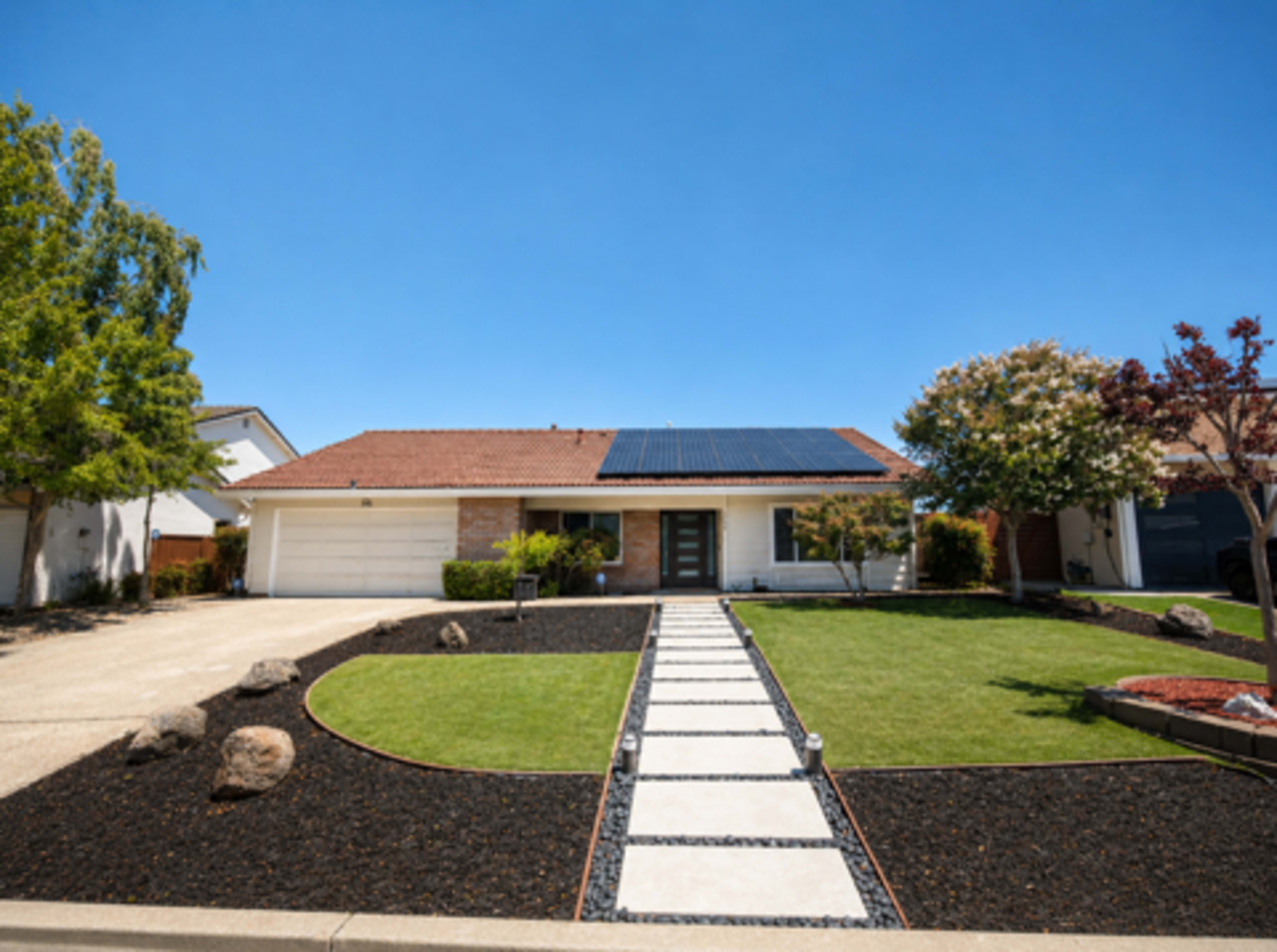The scene shows a single-story house with a solar panel roof, a concrete walkway leading to the entrance, and landscaped yards featuring grass, decorative rocks, and shrubs.