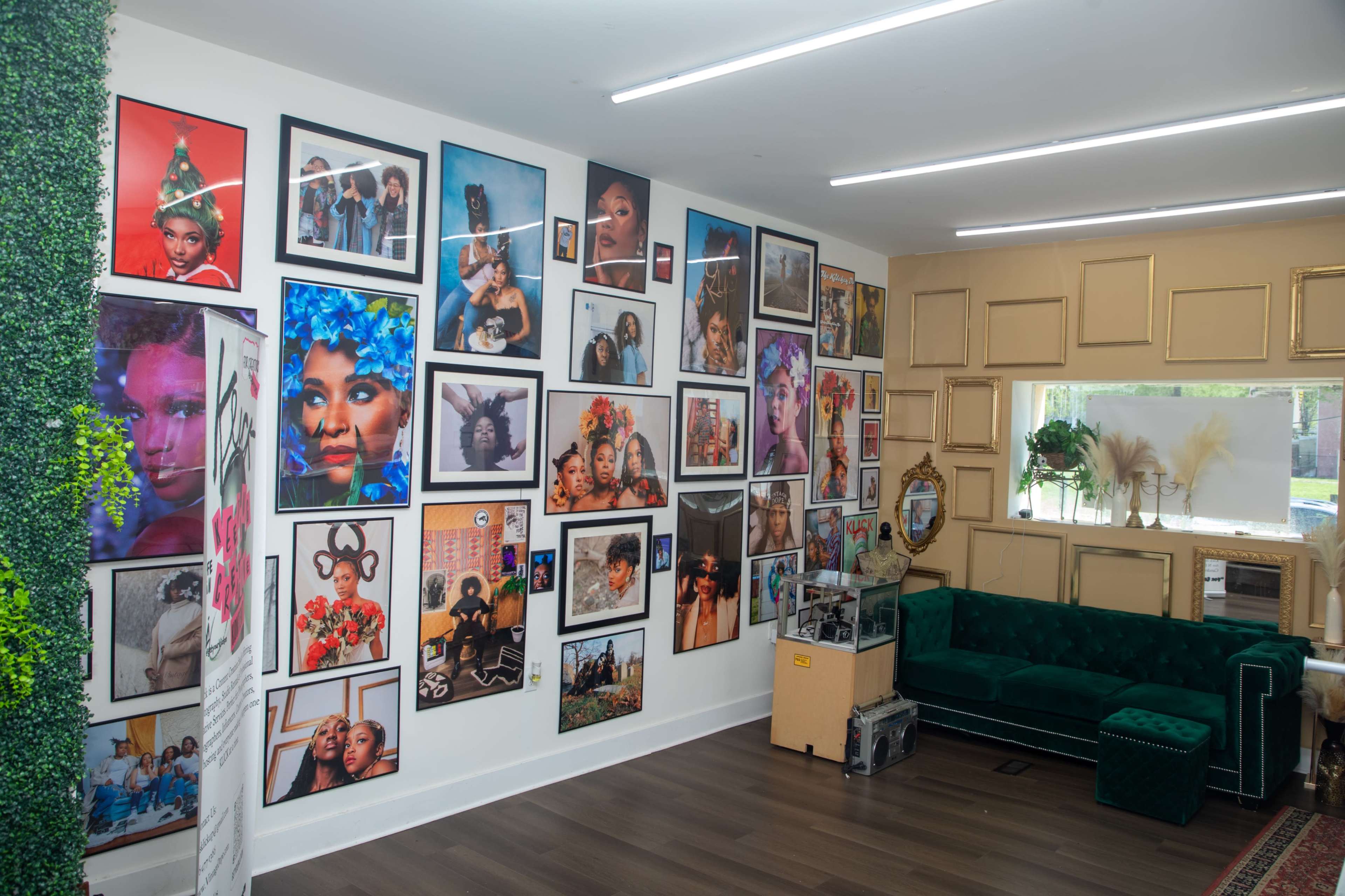 The image shows a room with a green velvet couch and walls adorned with various large framed photographs of diverse individuals, showcasing colorful hairstyles and makeup.