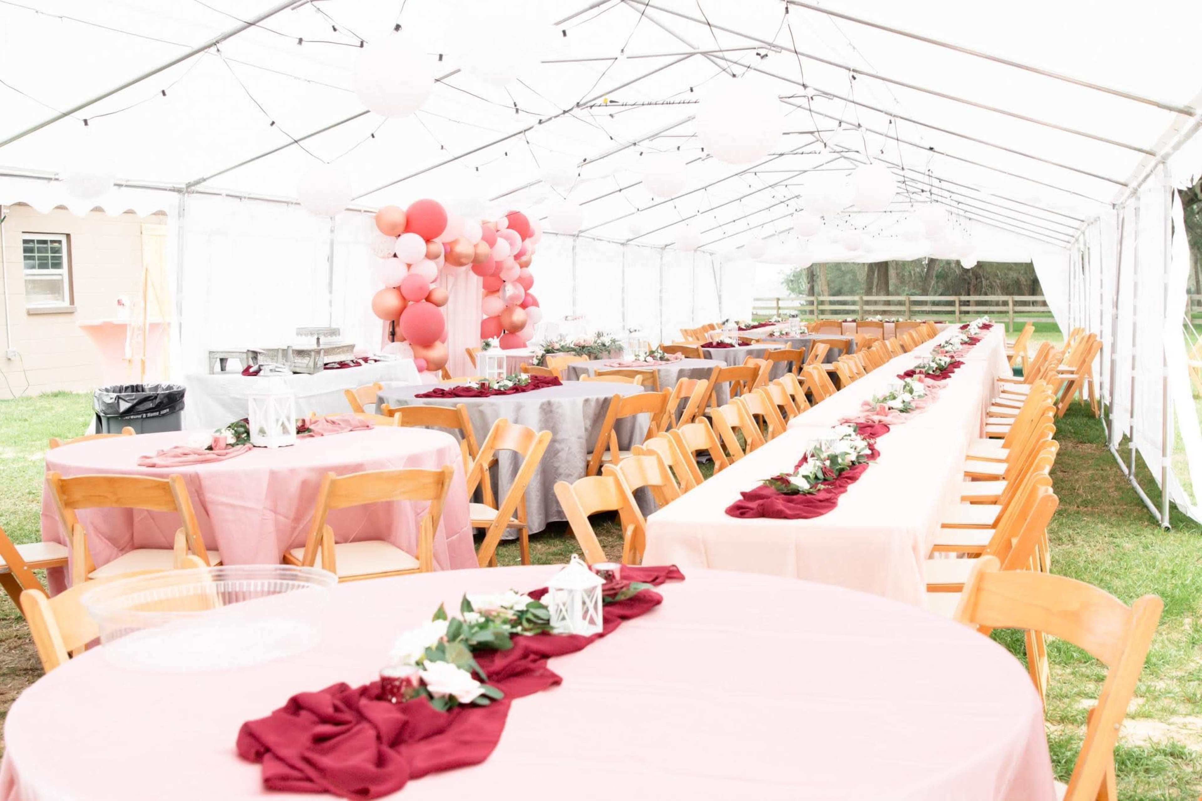 A large outdoor tent is set up for a banquet with rows of tables covered in various colored linens and decorated with floral centerpieces.