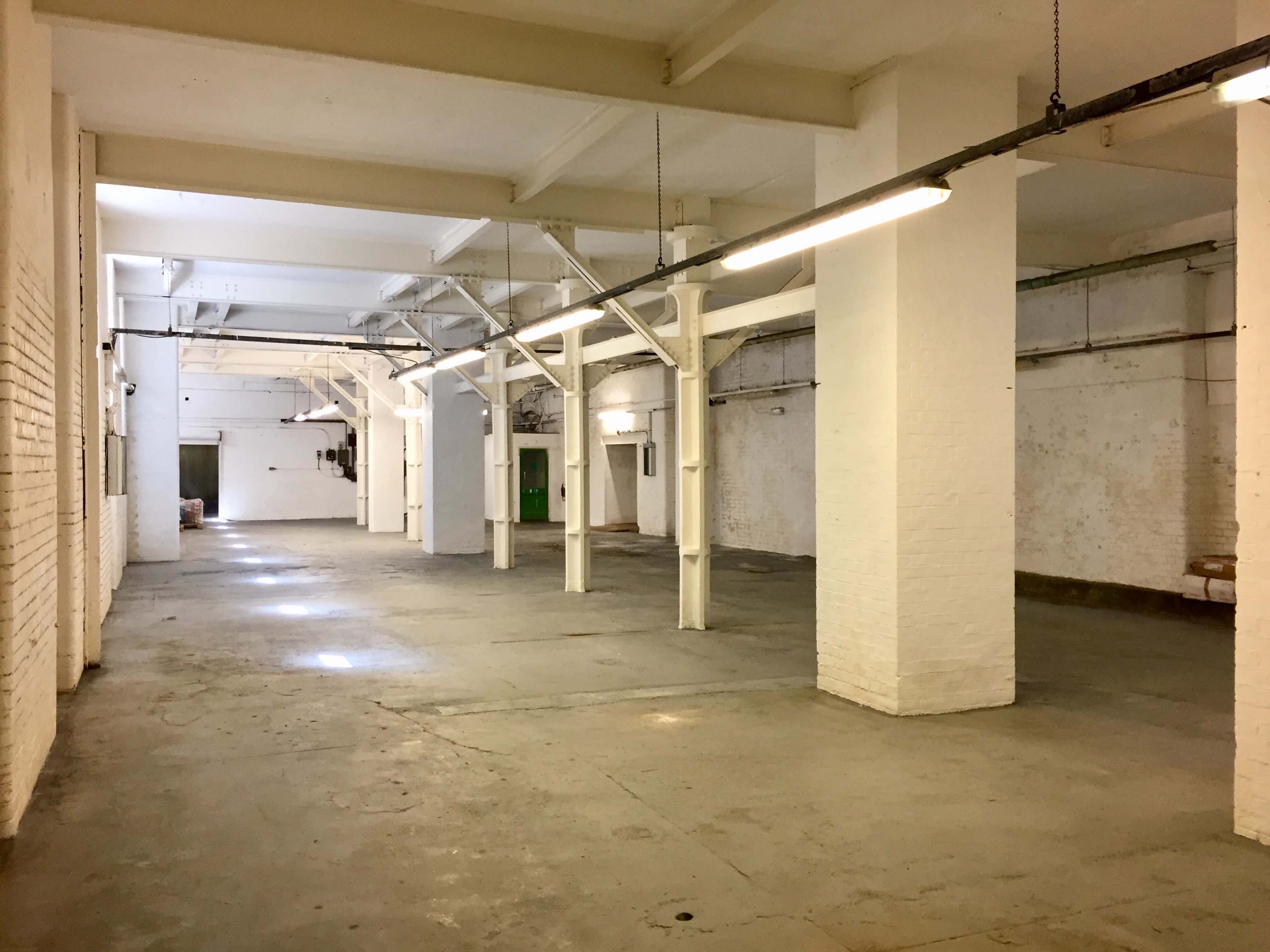 A large, empty industrial space with white walls, exposed beams, and overhead lights.