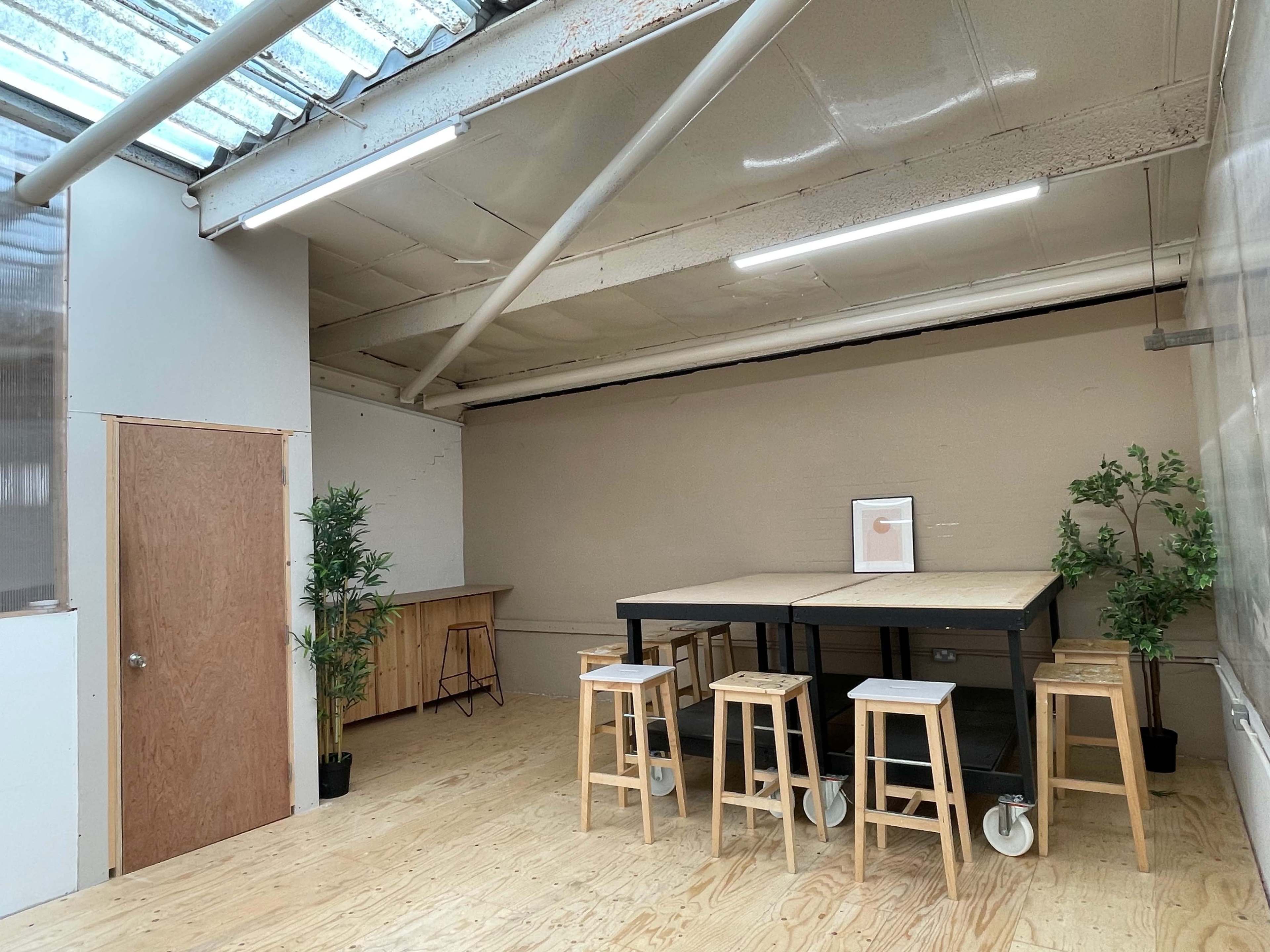 An interior space featuring a large table with stools, two plants, and a door leading to another room.