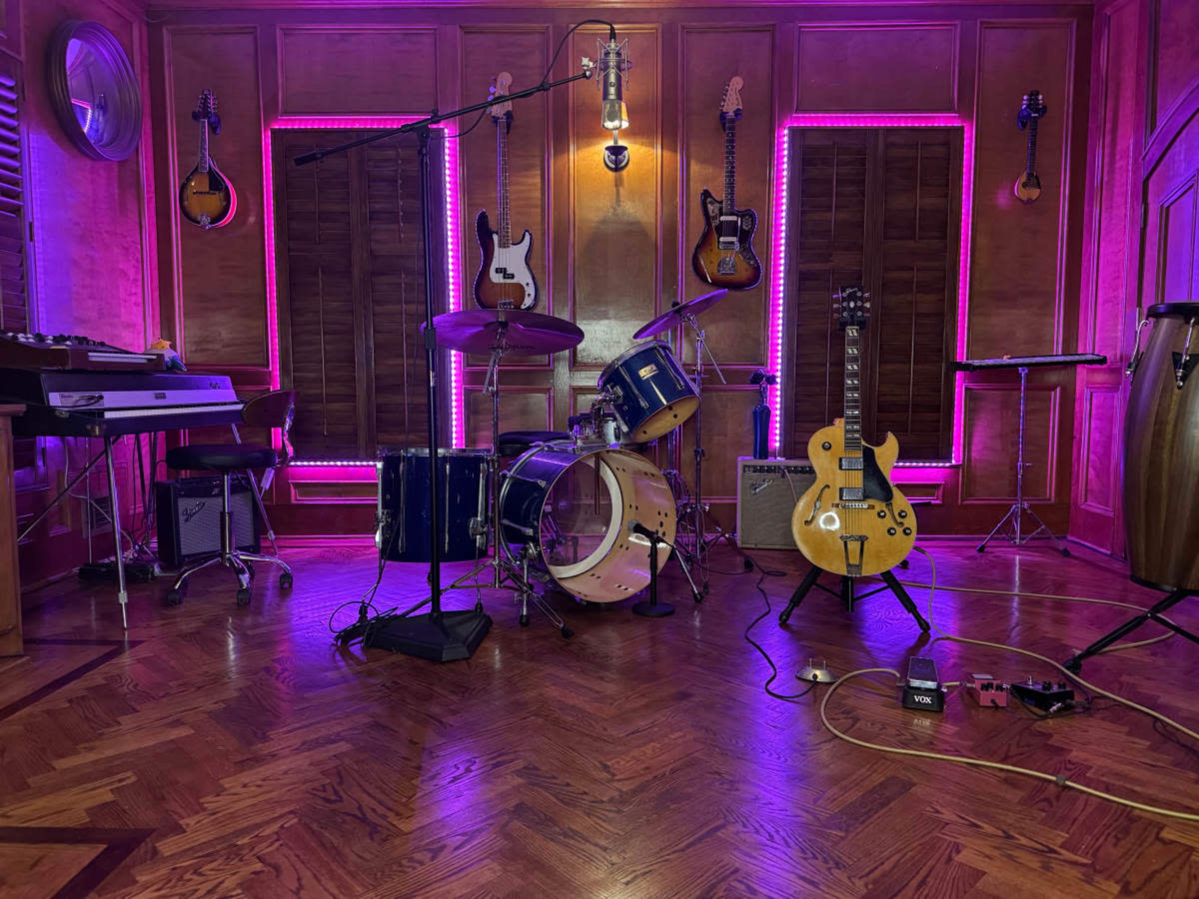 The image shows a music studio with various instruments including guitars, drums, and a keyboard, illuminated by purple LED lights.