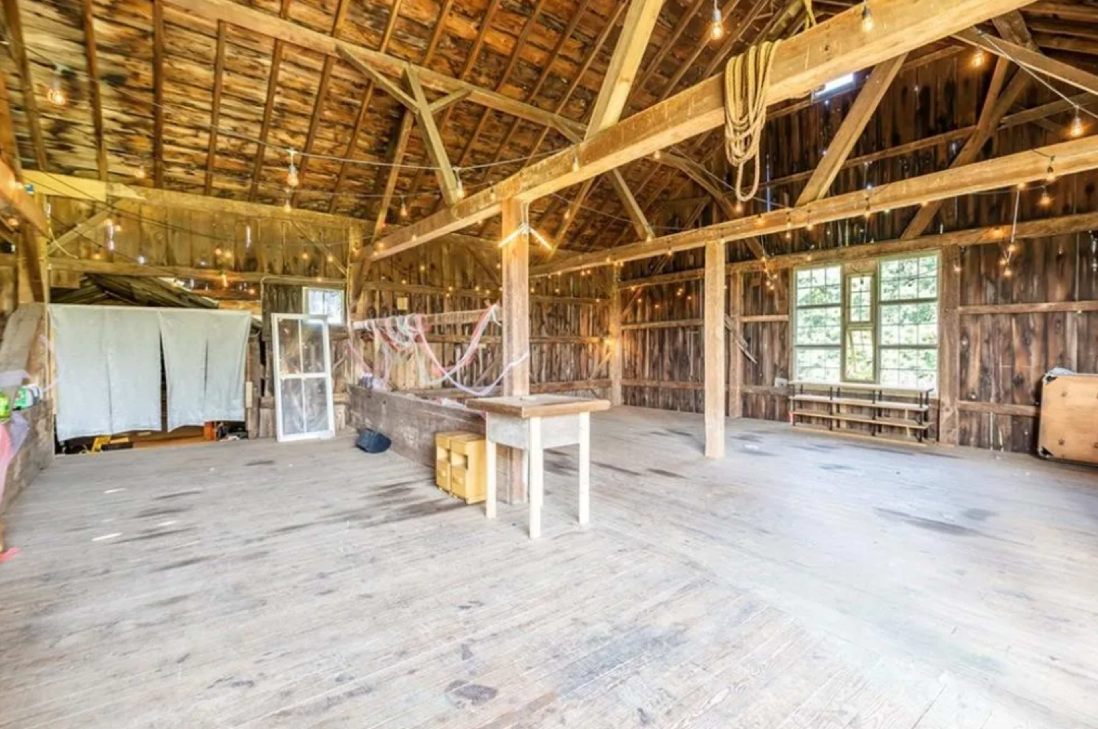 The interior of a rustic barn with wooden walls, a high ceiling, and a spacious wooden floor, featuring simple furniture and decor.