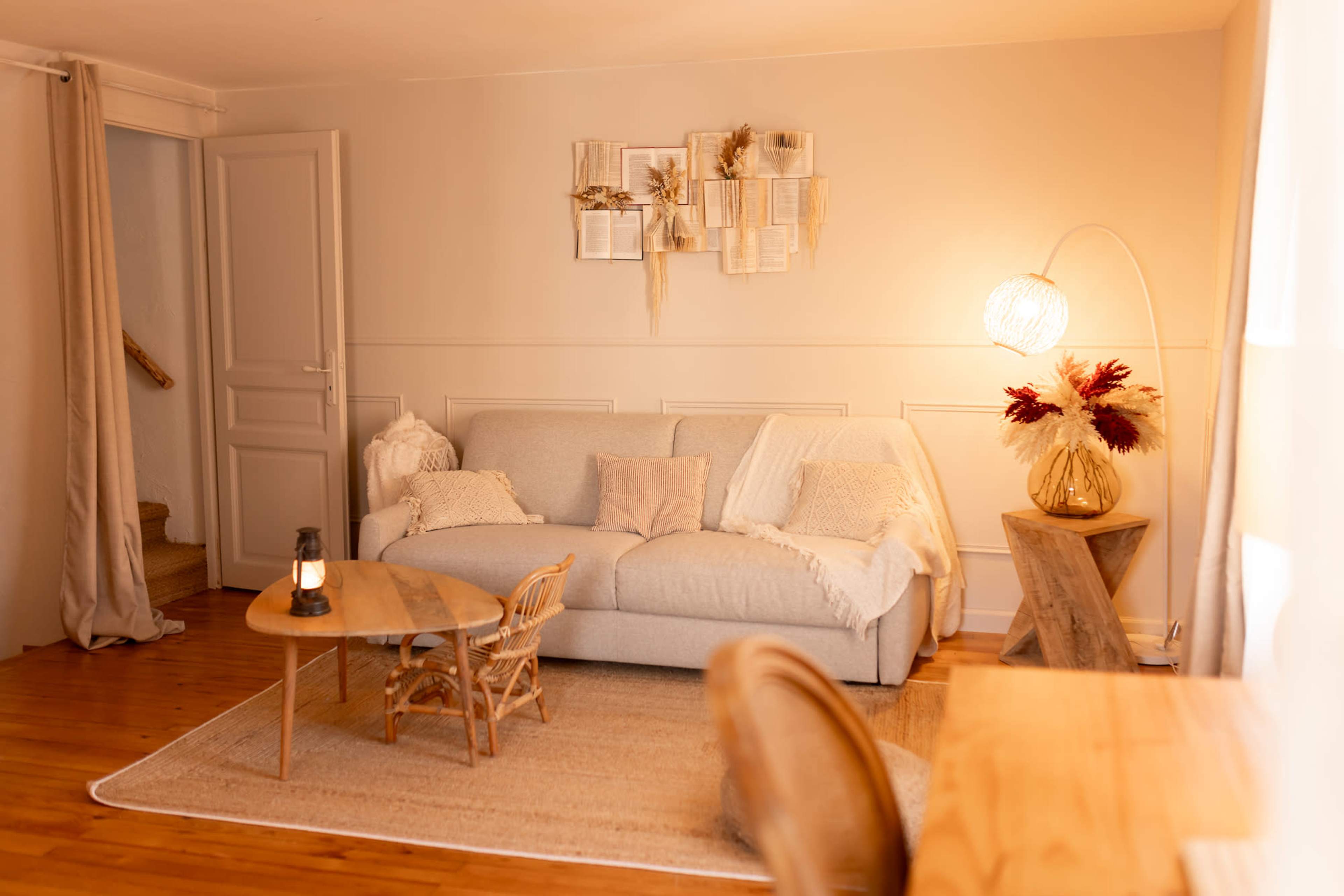 The image shows a cozy living room with a light gray sofa, a wooden coffee table, and decorative elements such as a floor lamp and plants.